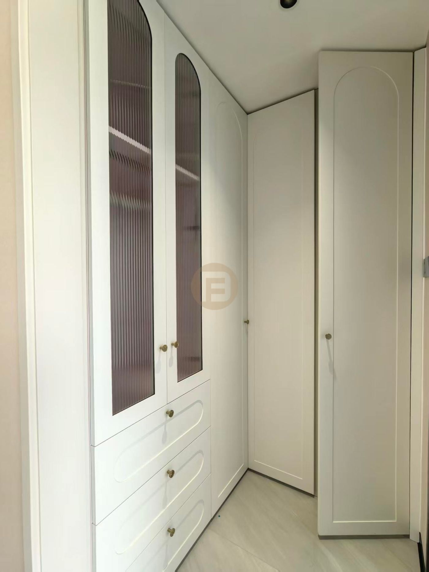 Cream arched wardrobes with reeded-glass doors and brass knobs lining a walk-in closet corner