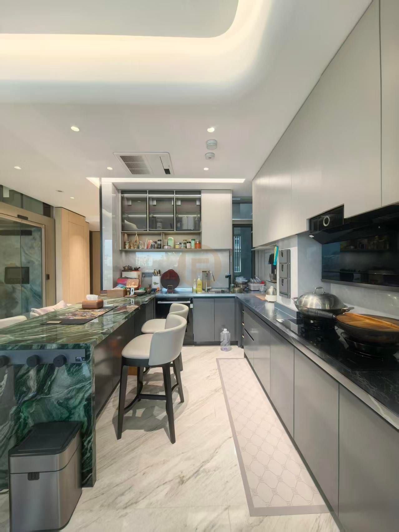 Green marble breakfast bar with grey stainless steel cabinetry and black cooktop run in an open kitchen