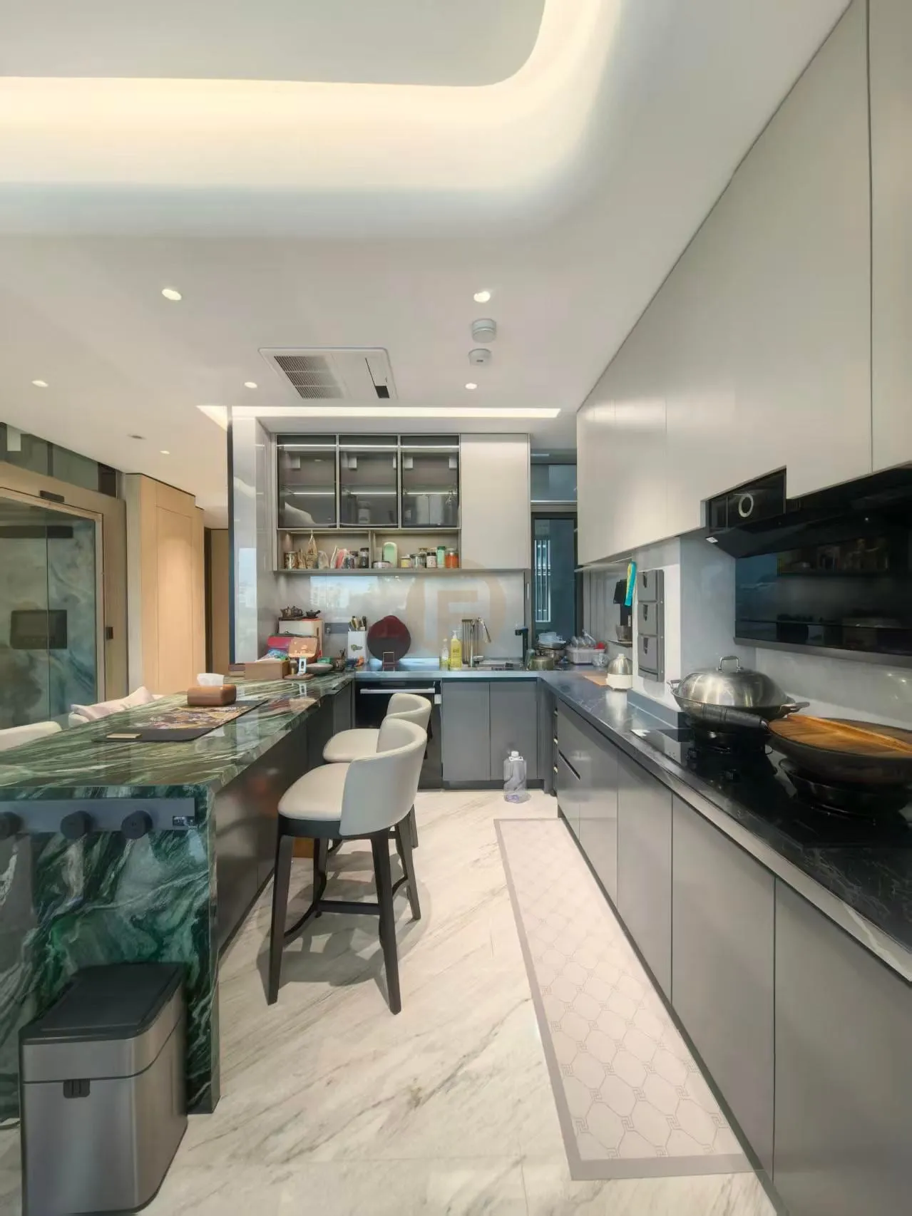 Green marble breakfast bar with grey stainless steel cabinetry and black cooktop run in an open kitchen