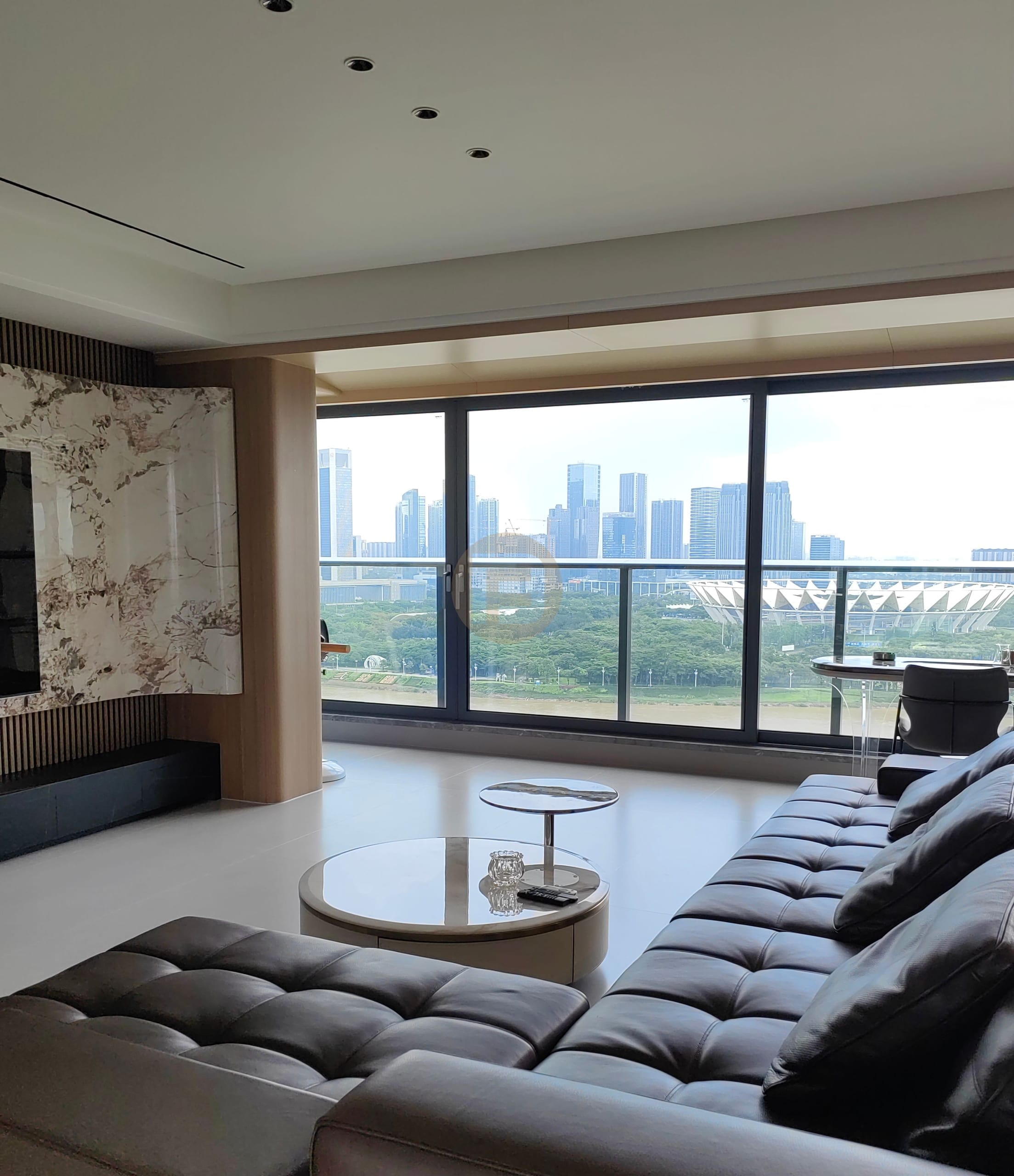 Living room with leather sectional, book-matched marble media wall and floor-to-ceiling city skyline glazing