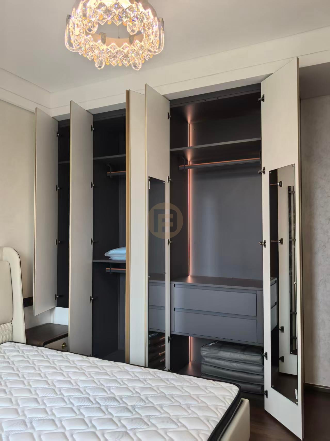 Open stainless steel wardrobe doors revealing lit interiors with drawers, rails and mirror panel
