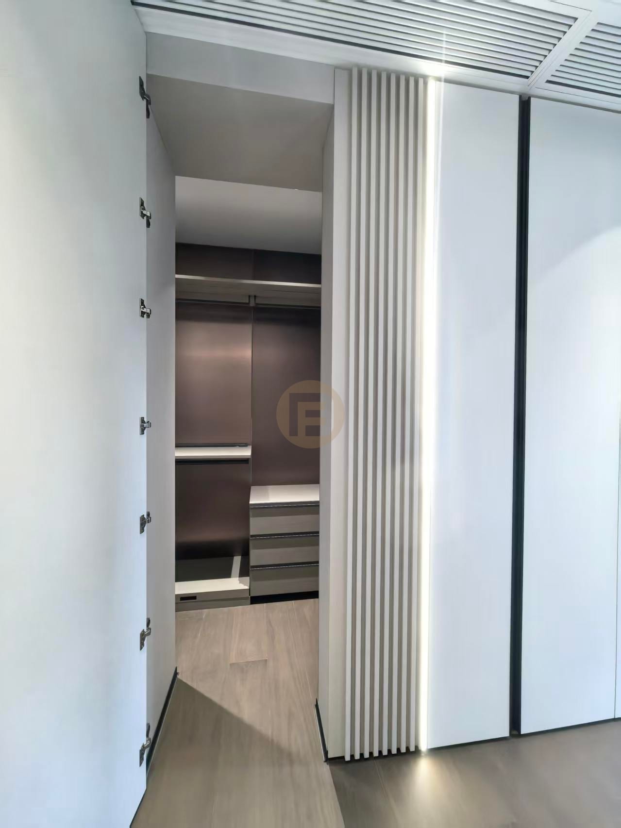 View through a backlit fluted panel into a walk-in closet with dark stainless steel wardrobe interior