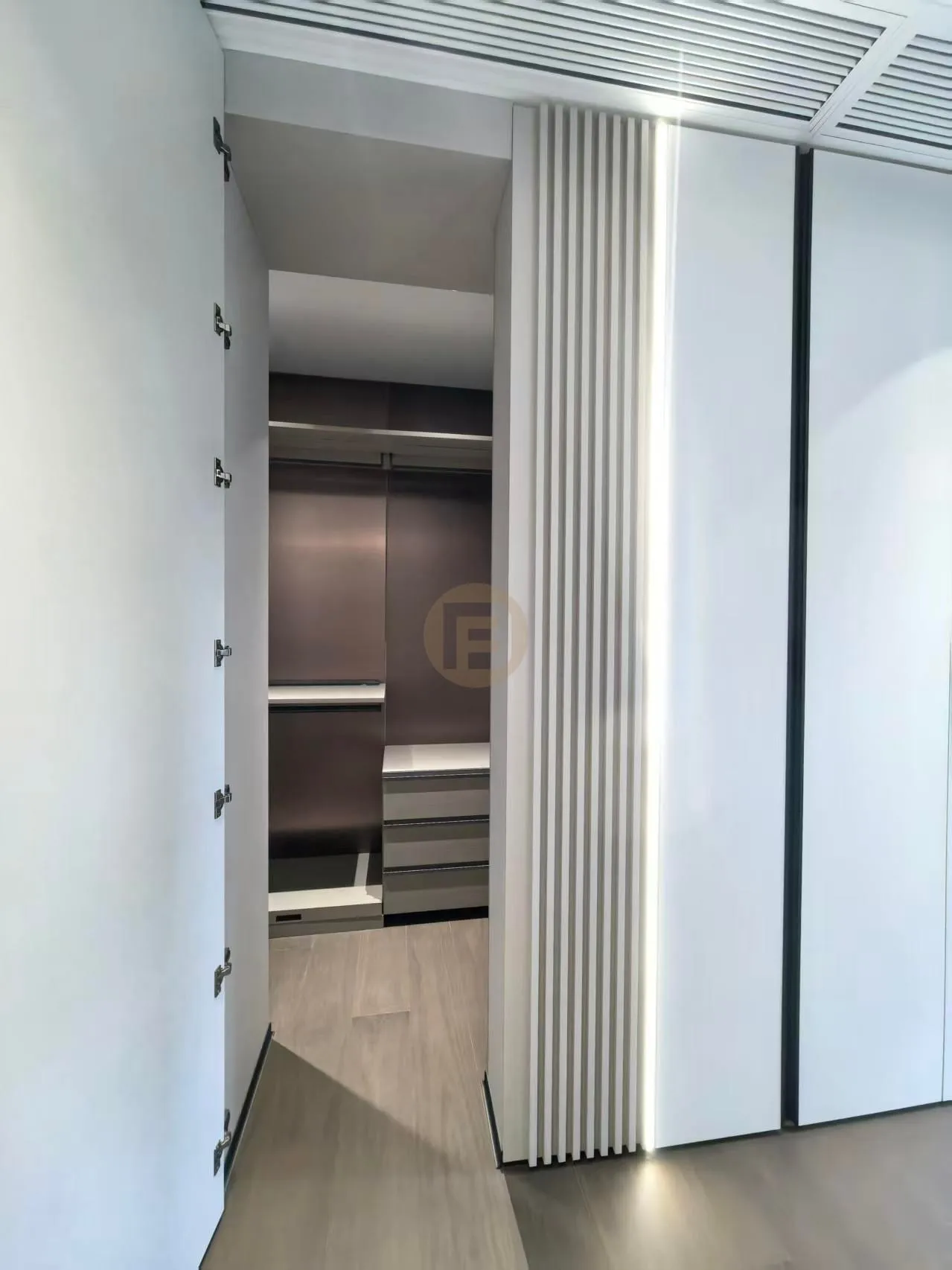 View through a backlit fluted panel into a walk-in closet with dark stainless steel wardrobe interior