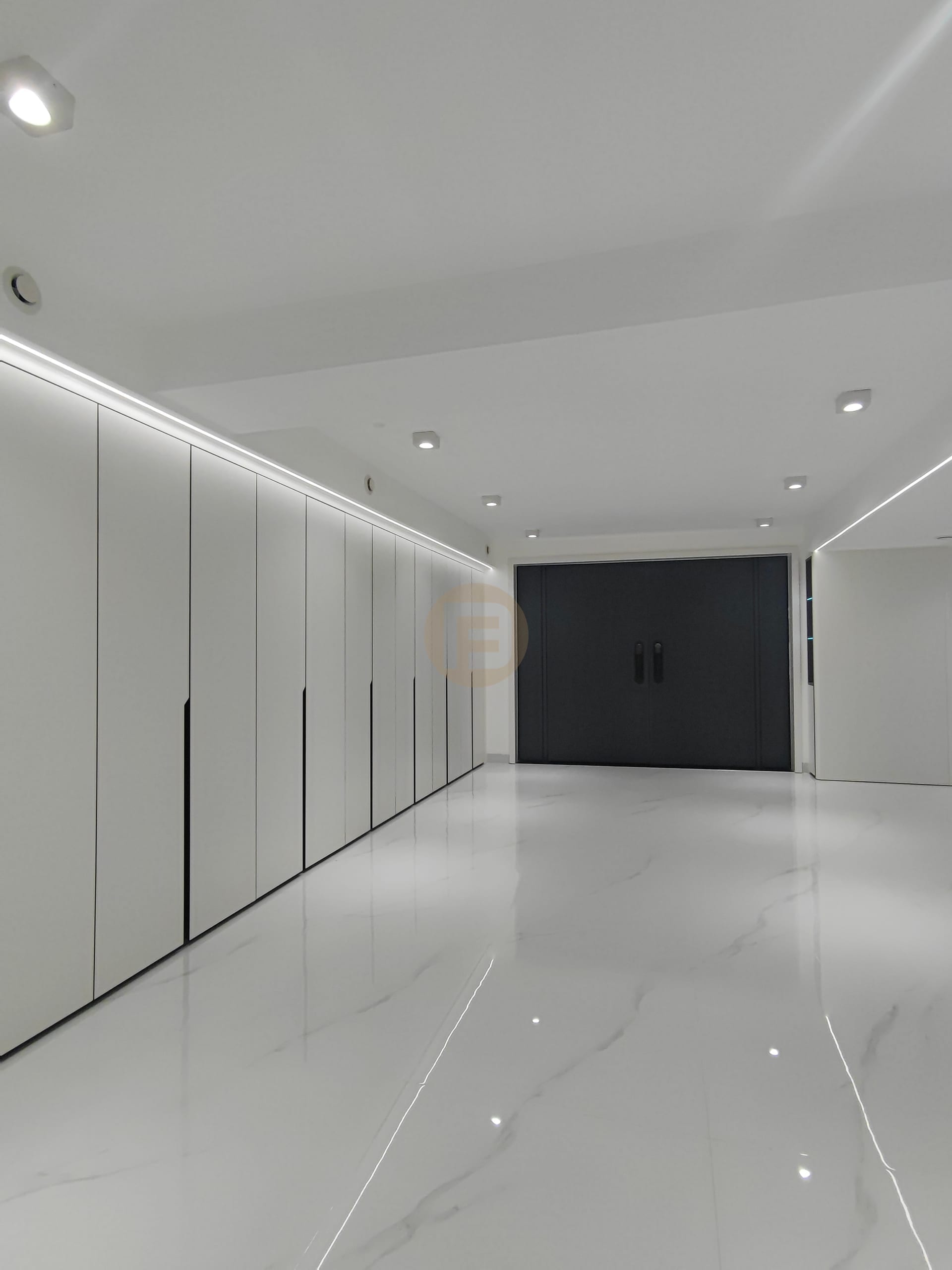 Corridor of white floor-to-ceiling stainless steel wardrobes with LED lighting leading to dark double doors