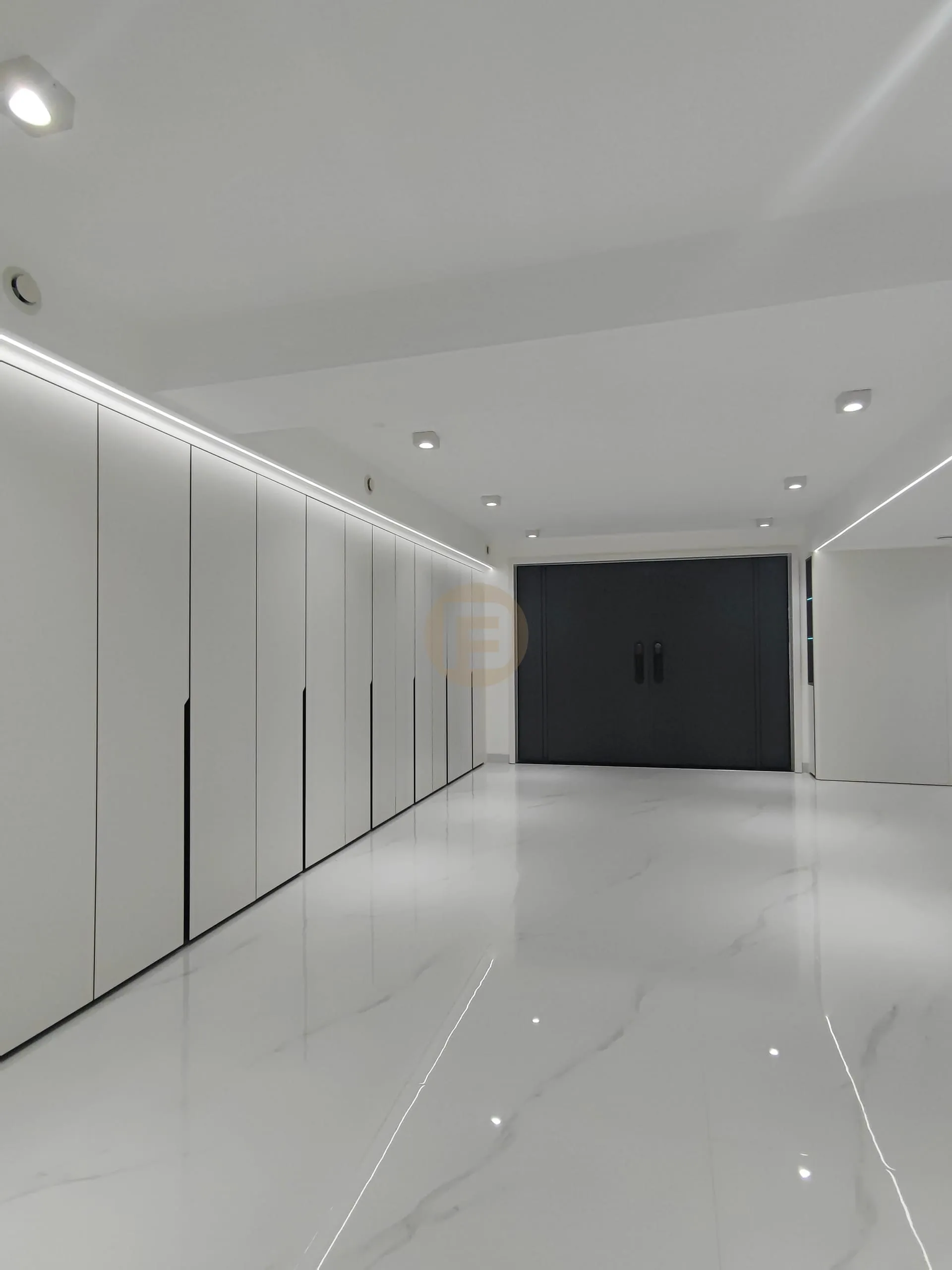 Corridor of white floor-to-ceiling stainless steel wardrobes with LED lighting leading to dark double doors