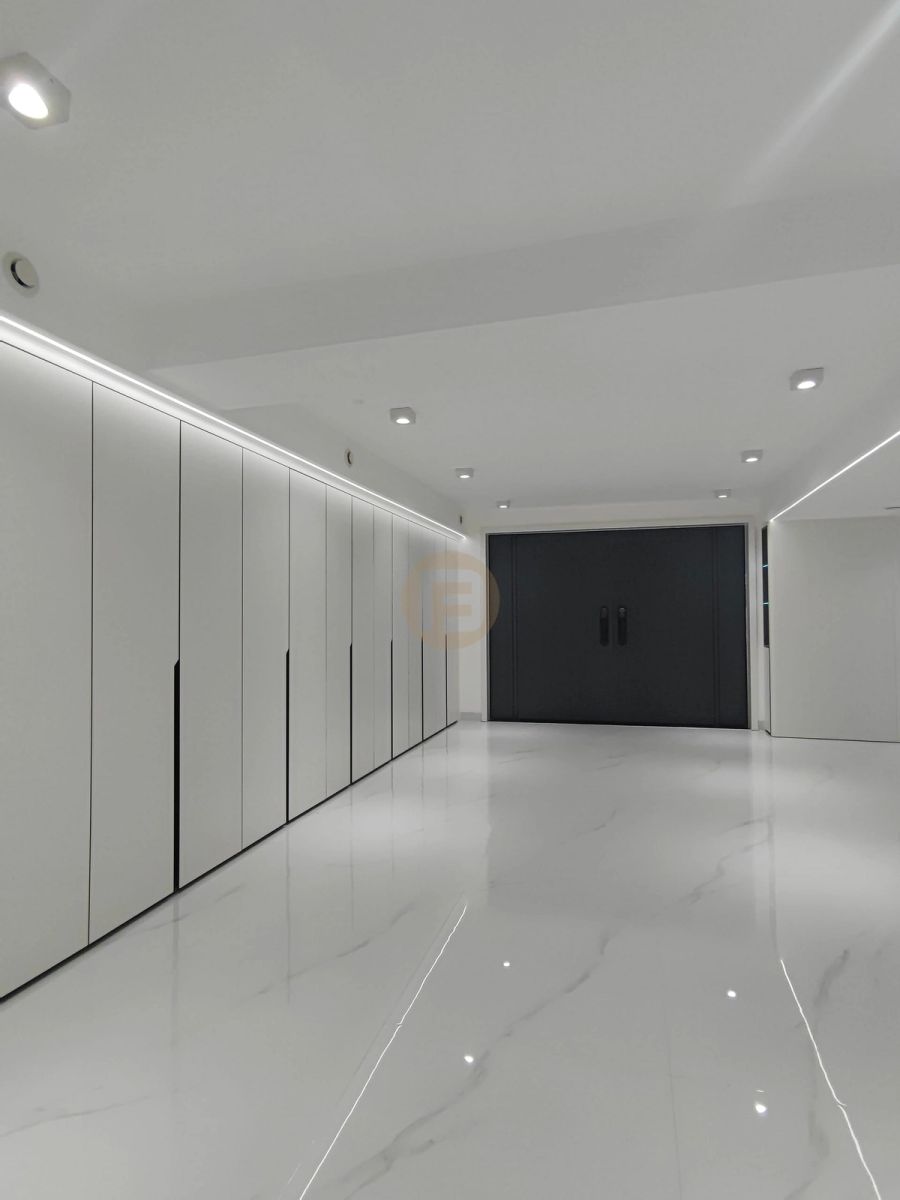 Corridor of white floor-to-ceiling stainless steel wardrobes with LED lighting leading to dark double doors