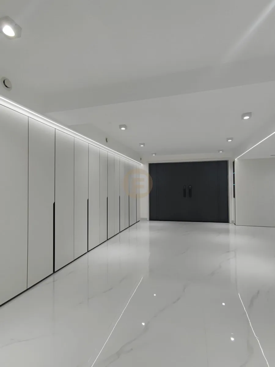 Corridor of white floor-to-ceiling stainless steel wardrobes with LED lighting leading to dark double doors