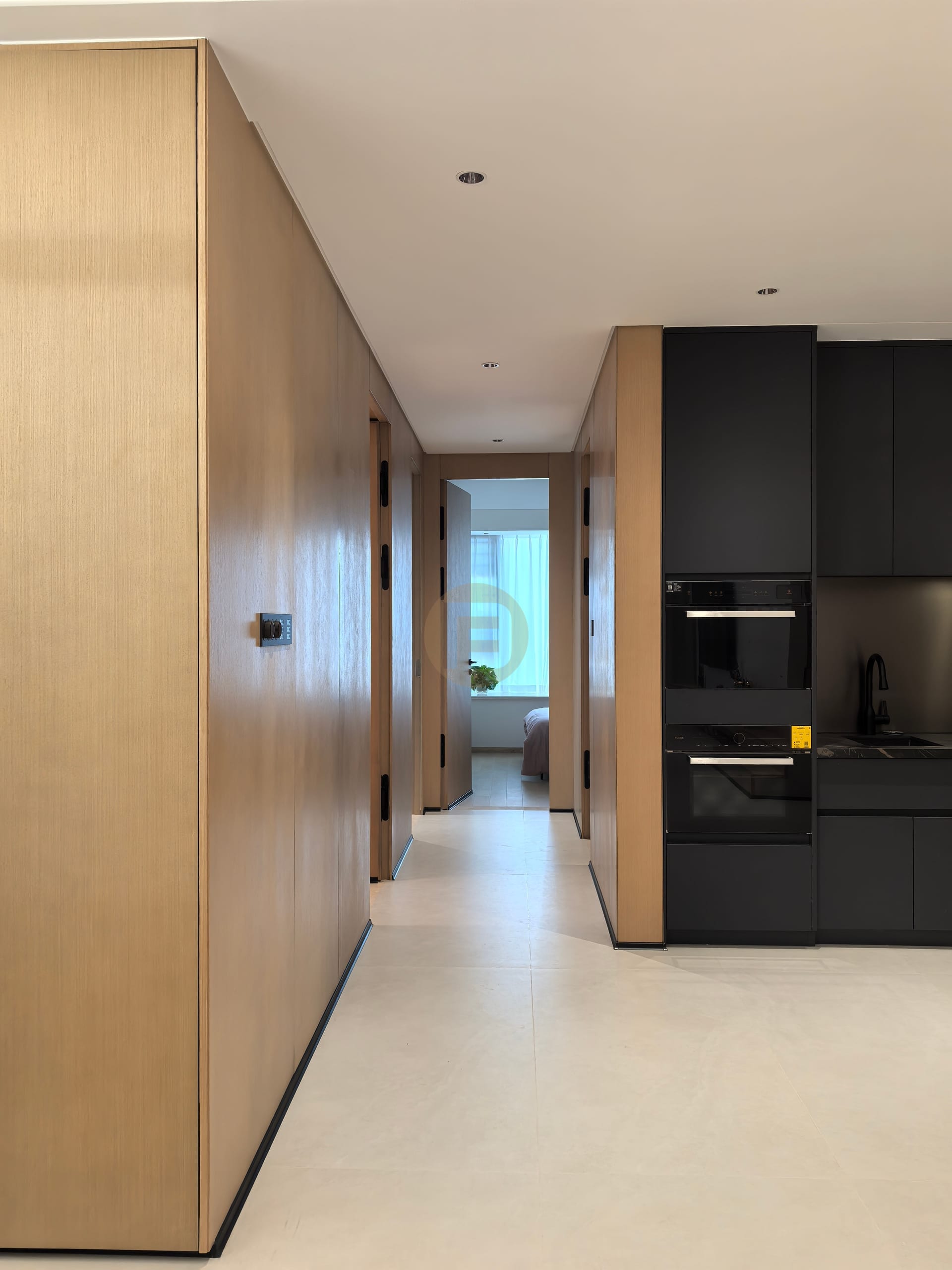 Oak-panelled cabinetry corridor leading past black kitchen units toward a bedroom suite