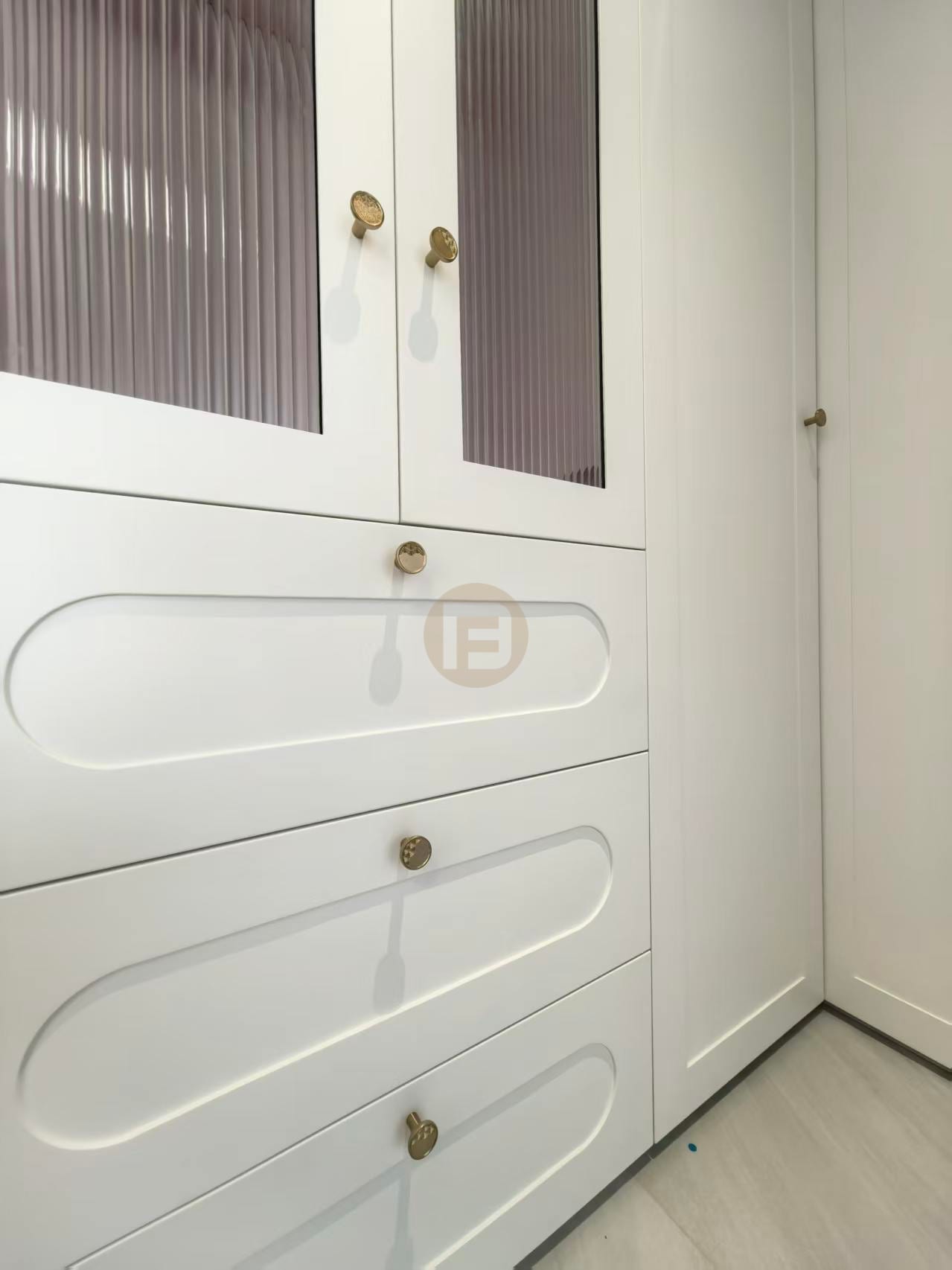 Detail of cream stainless steel cabinetry with reeded-glass doors, recessed drawer profiles and brass hardware