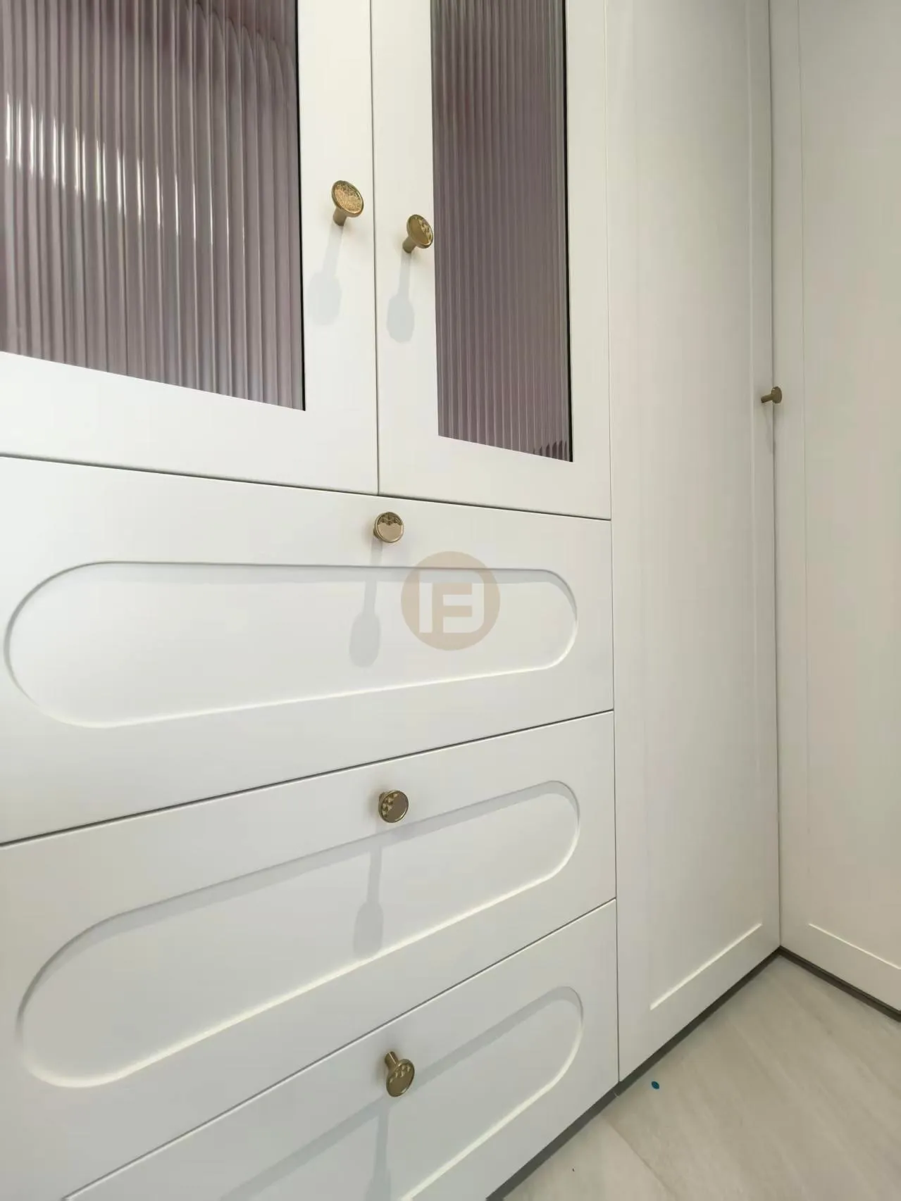 Detail of cream stainless steel cabinetry with reeded-glass doors, recessed drawer profiles and brass hardware
