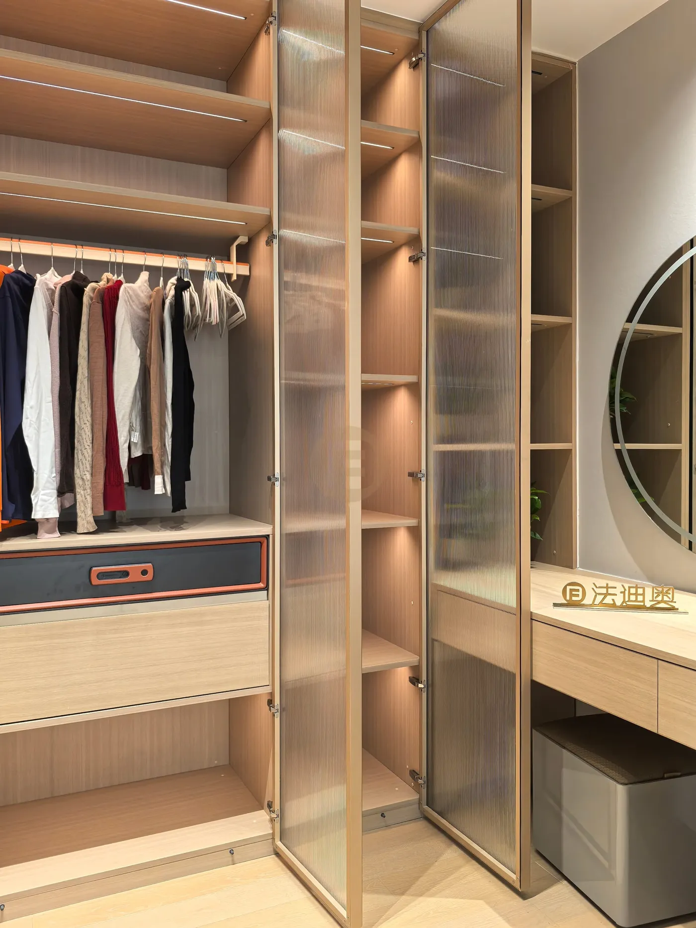 Walk-in closet with champagne fluted-glass doors, lit shelving and a built-in vanity with round mirror