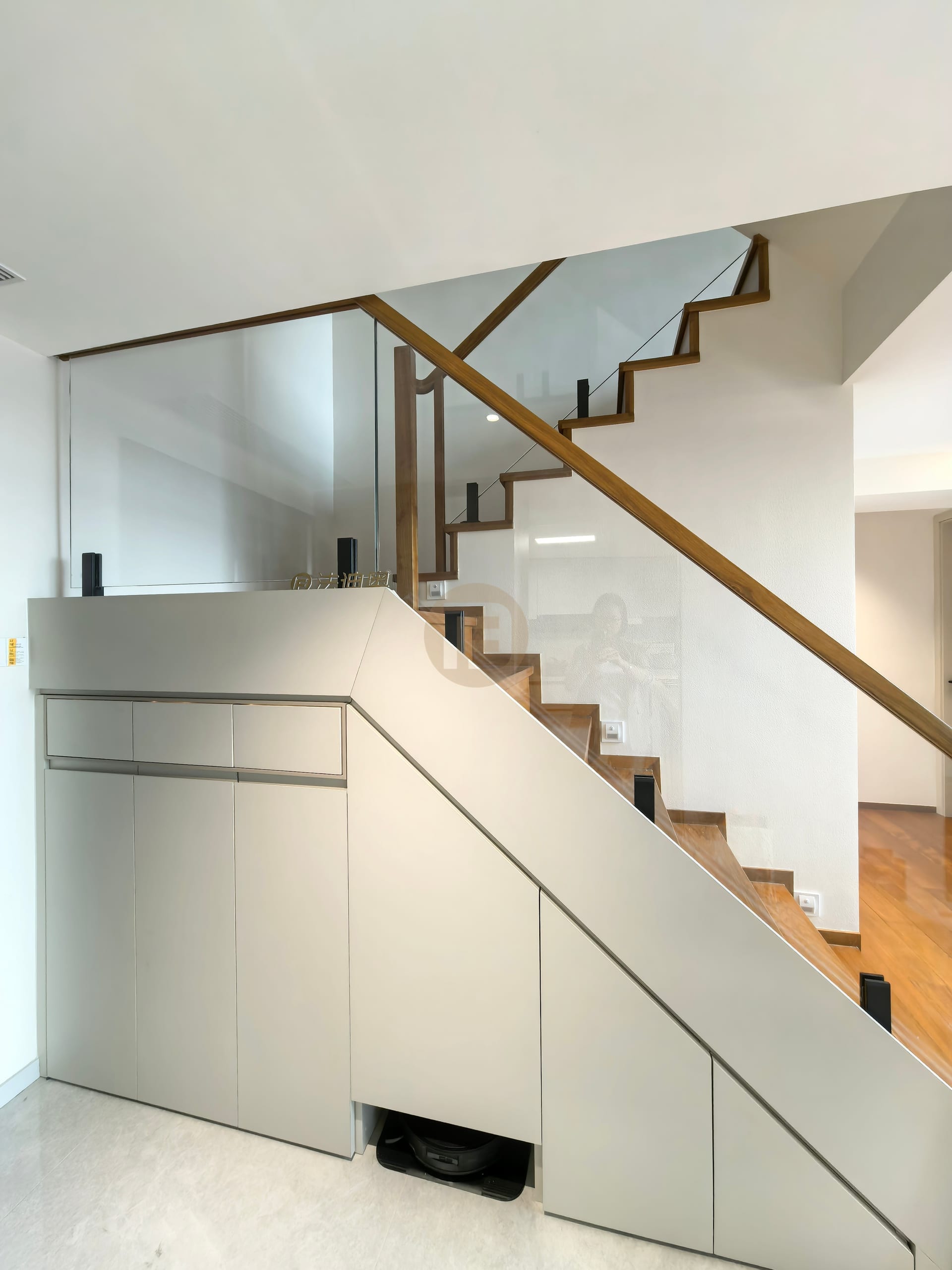 Under-stair storage cabinetry in warm grey stainless steel beneath a timber and glass staircase