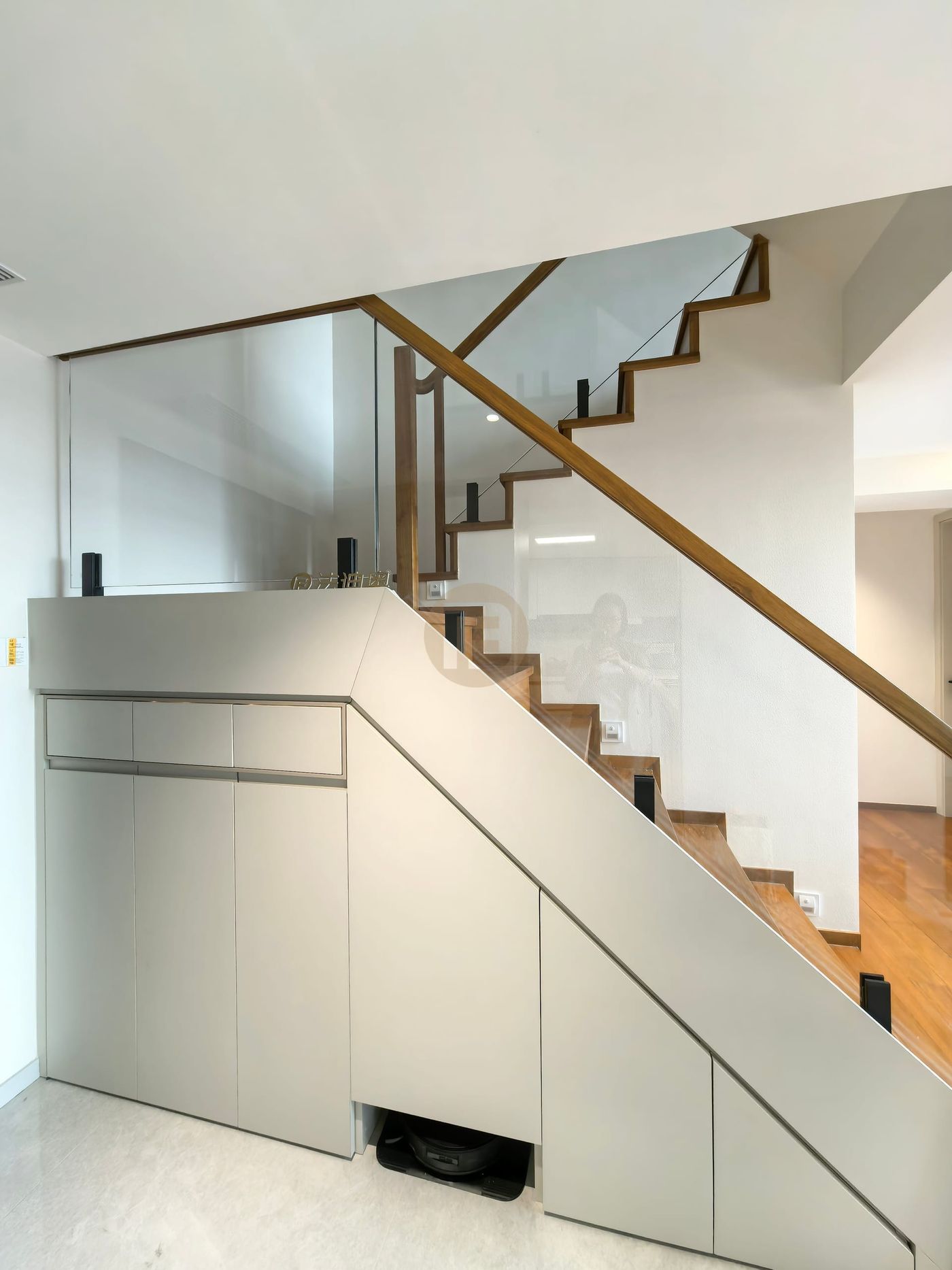 Under-stair storage cabinetry in warm grey stainless steel beneath a timber and glass staircase