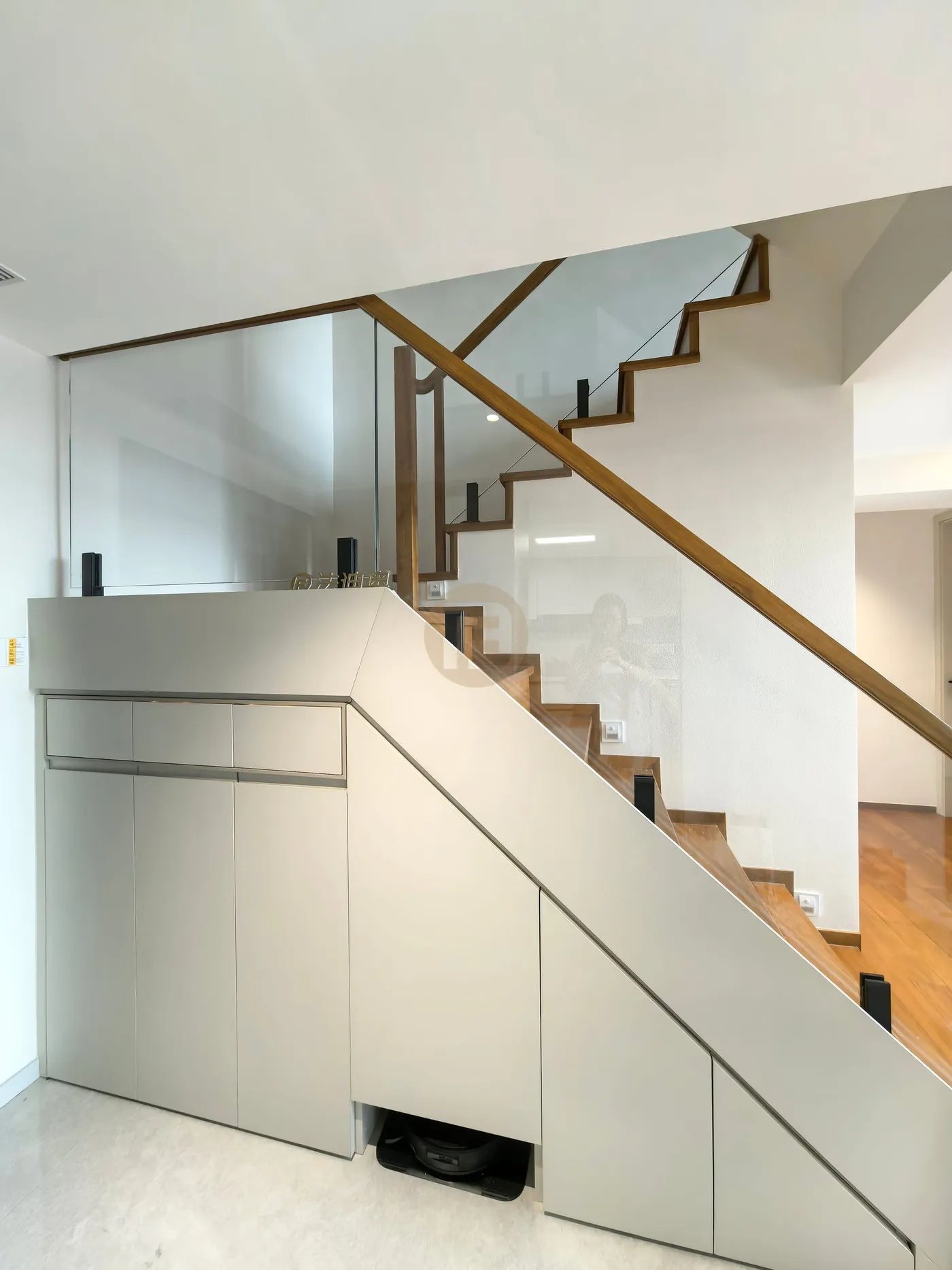 Under-stair storage cabinetry in warm grey stainless steel beneath a timber and glass staircase