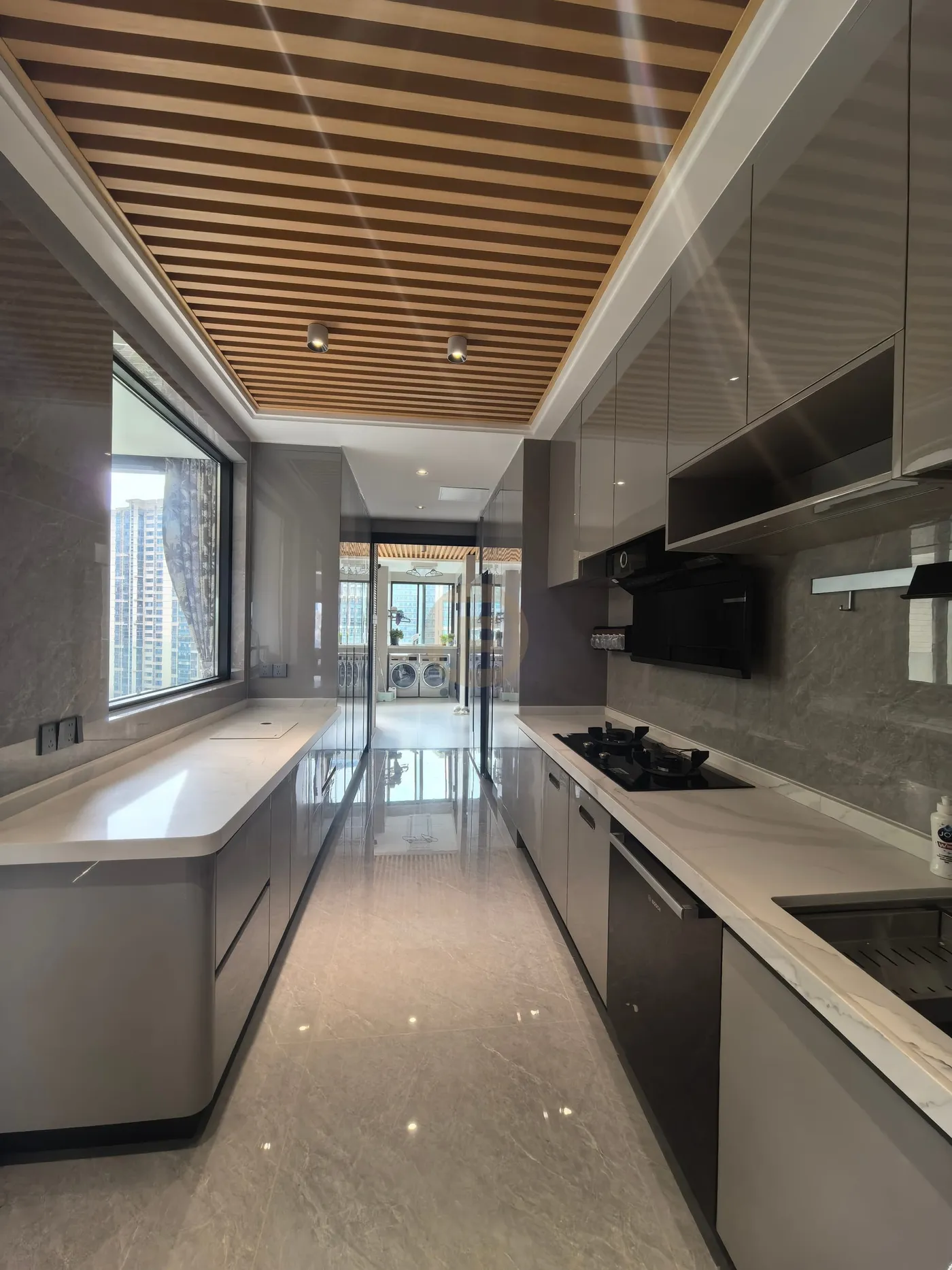 Galley kitchen with glossy grey stainless steel cabinetry under a timber-slat ceiling