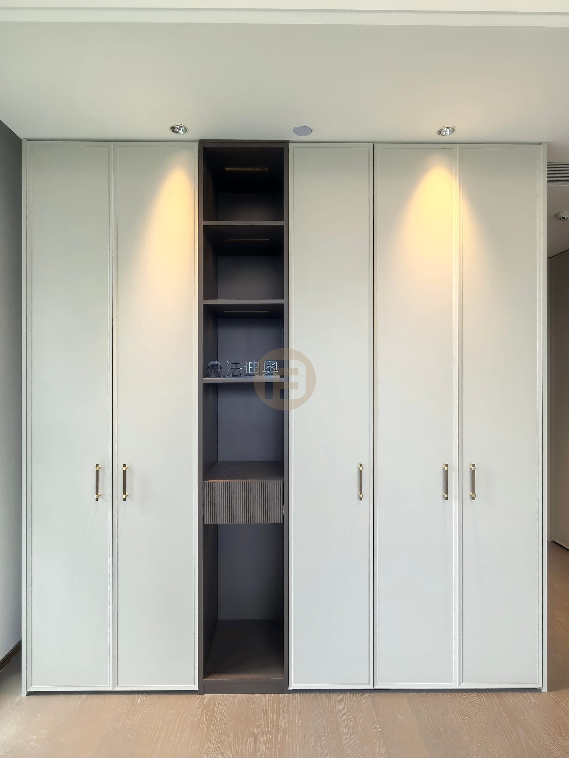 Symmetrical pale sage wardrobe wall with a dark open shelving column at its centre