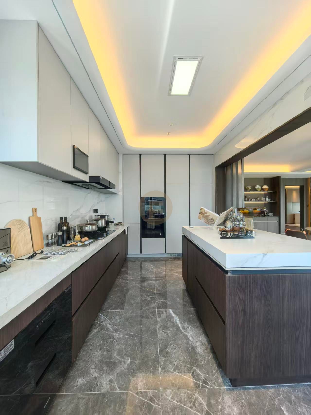 Galley view of the show kitchen with marble backsplash, island storage and warm cove lighting