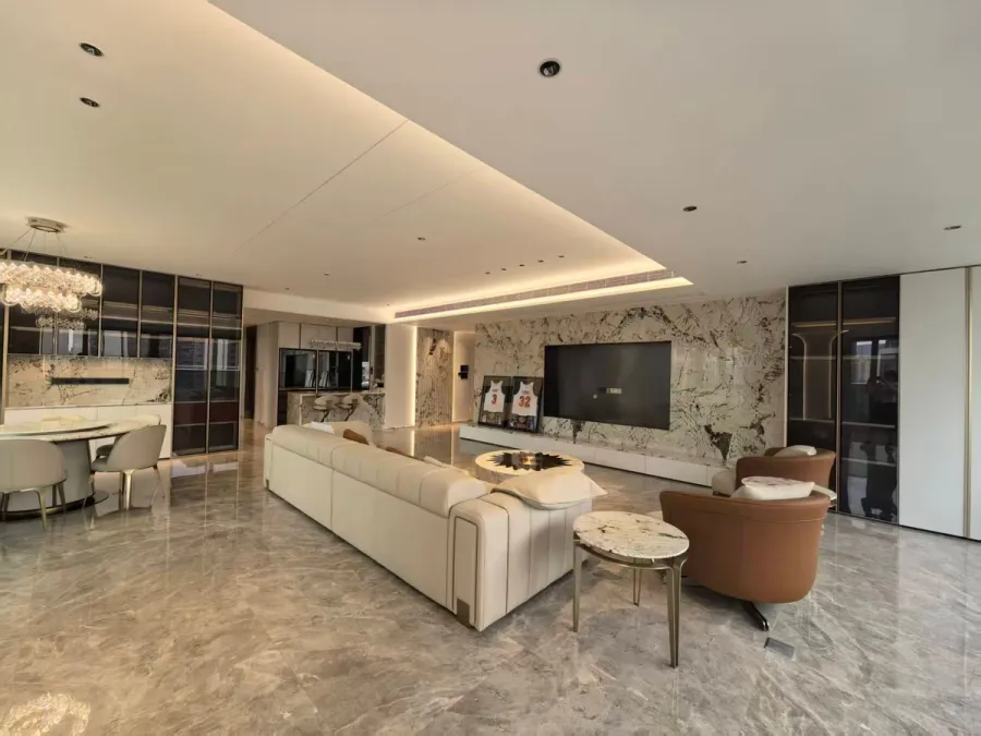 Open-plan living and dining room with bookmatched marble TV wall, cream sofas and bronze-glass display cabinetry