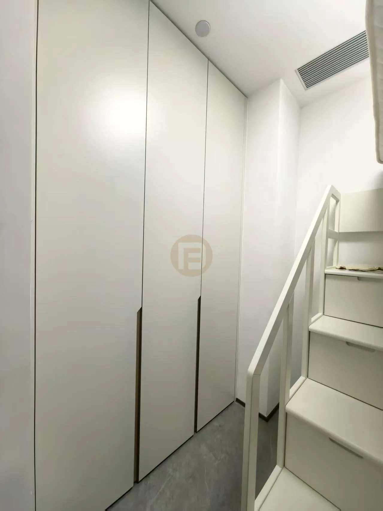Cream full-height stainless steel wardrobes fitted beside a white loft staircase
