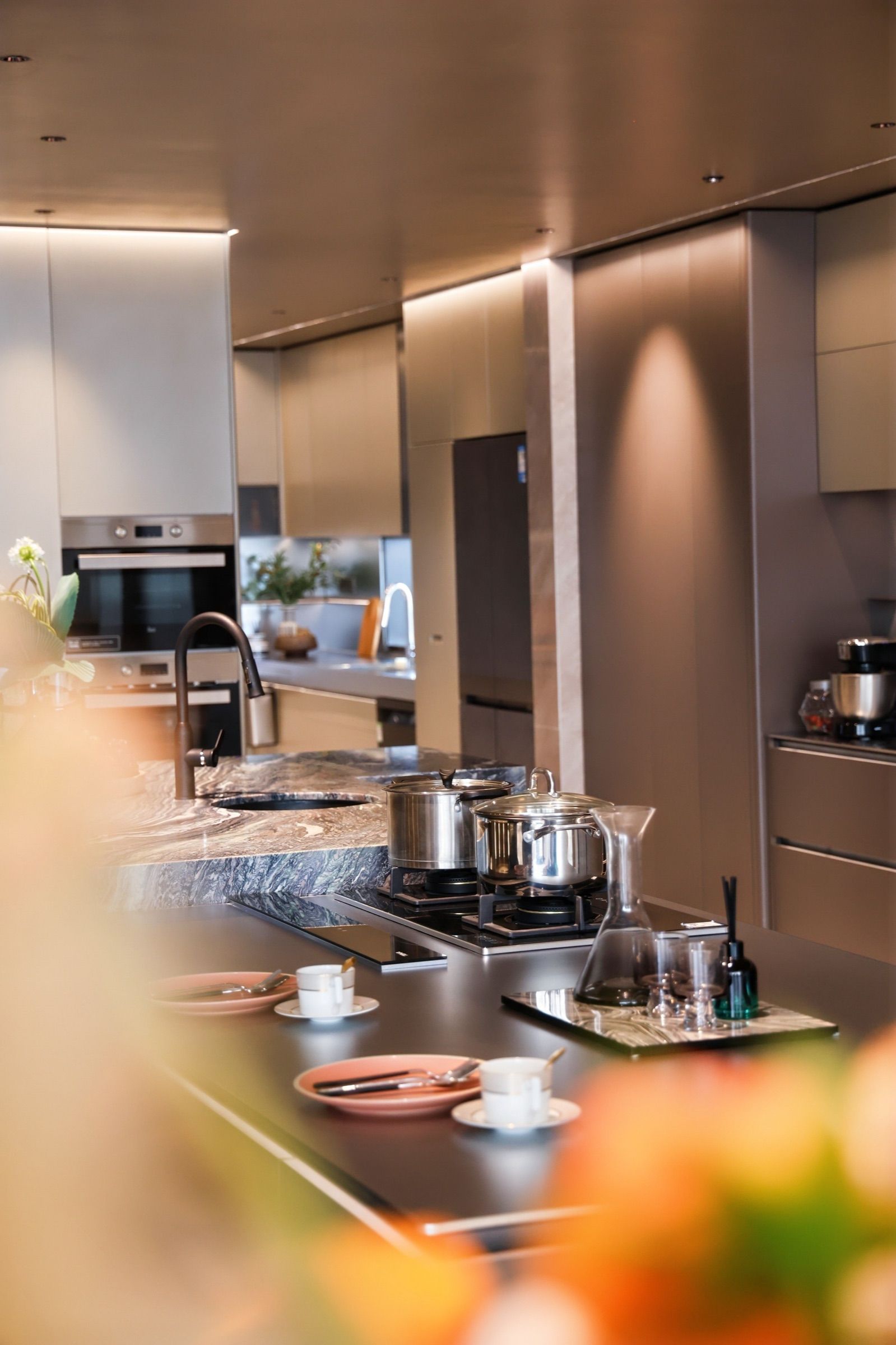 Close vertical view of stainless steel kitchen worktops, tall cabinets and integrated lighting.
