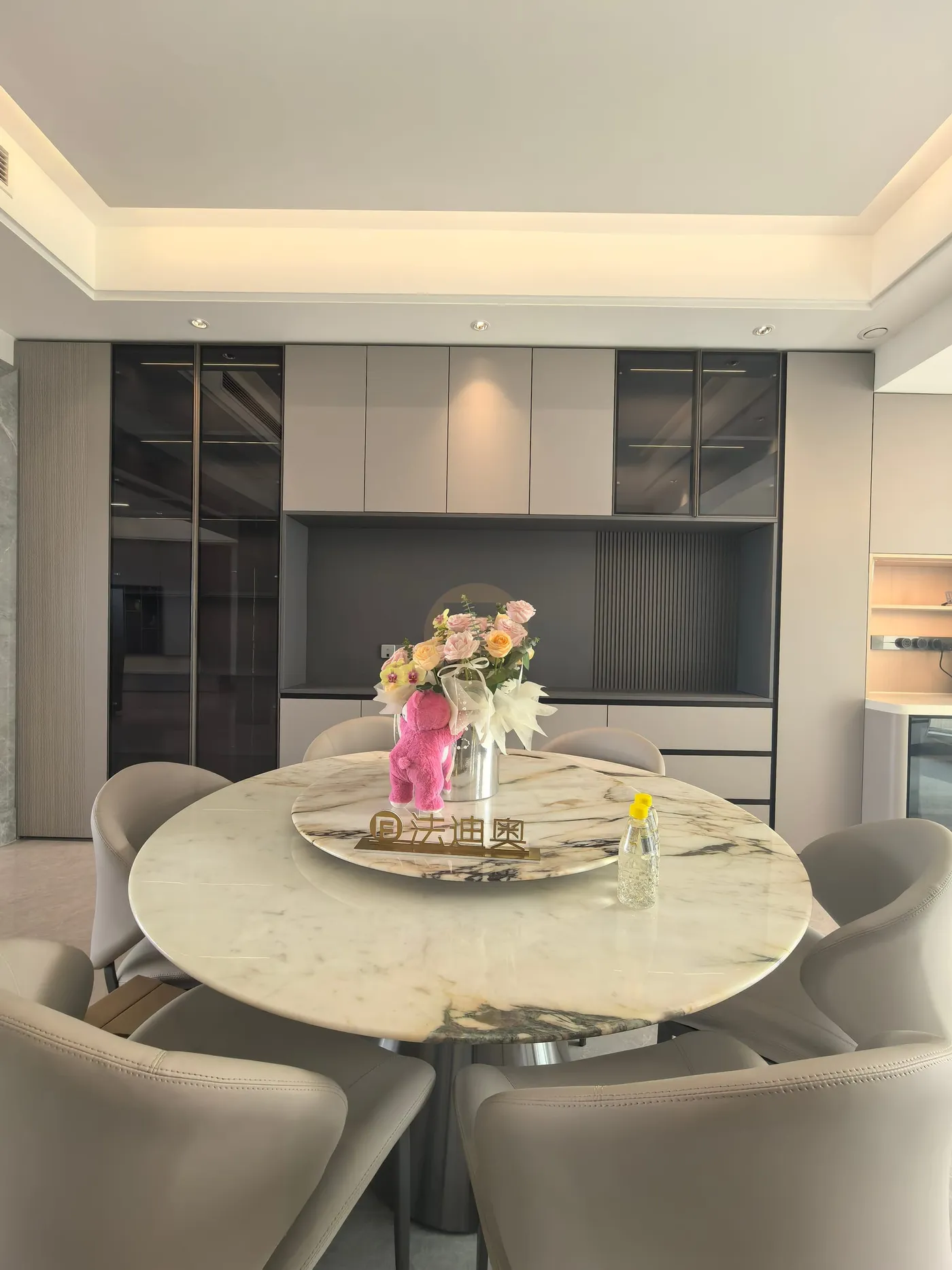 Dining room with round marble table and a glass-fronted stainless steel sideboard wall