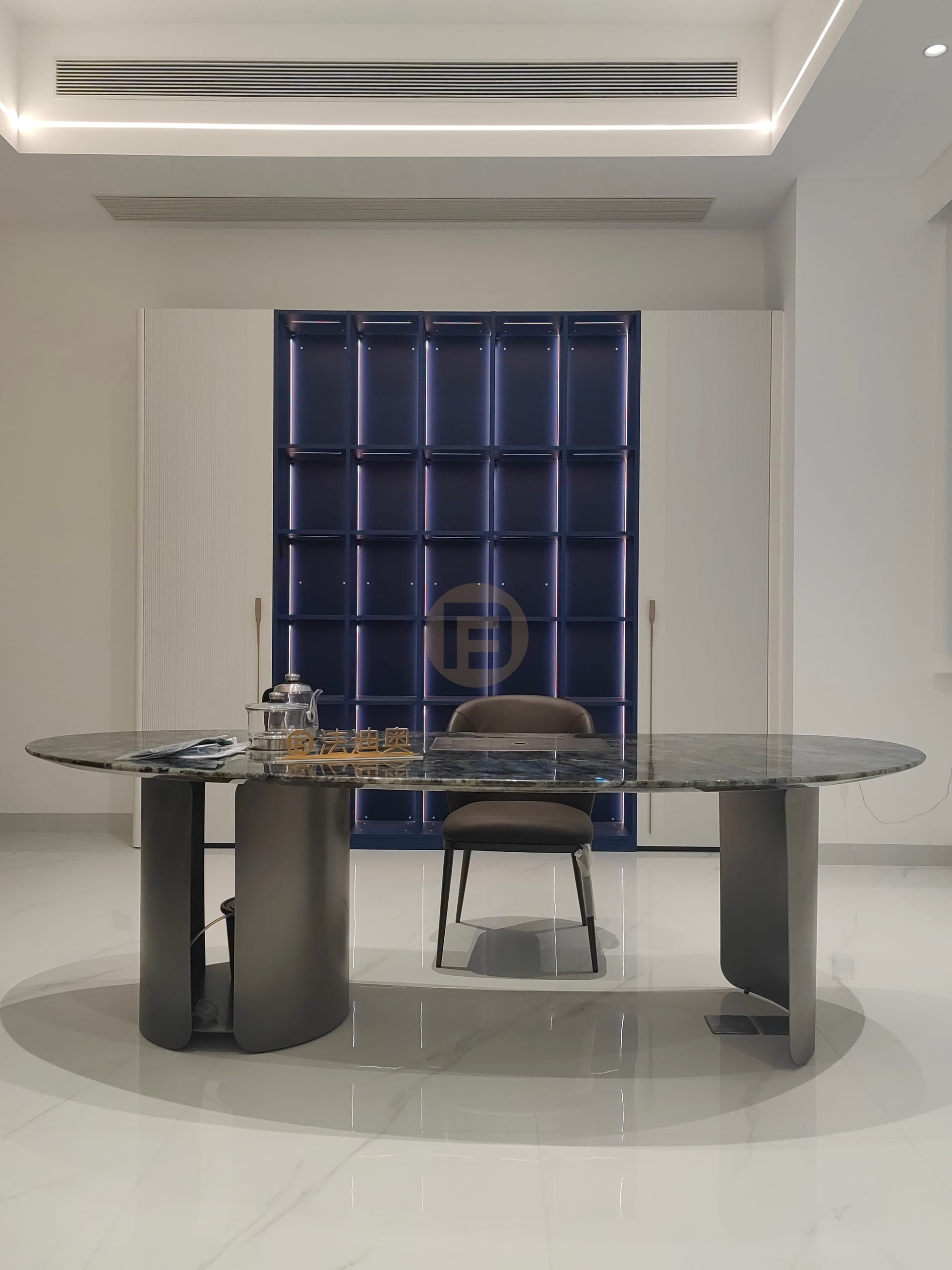 Study with green marble desk facing an illuminated navy display cabinet framed by white wardrobes