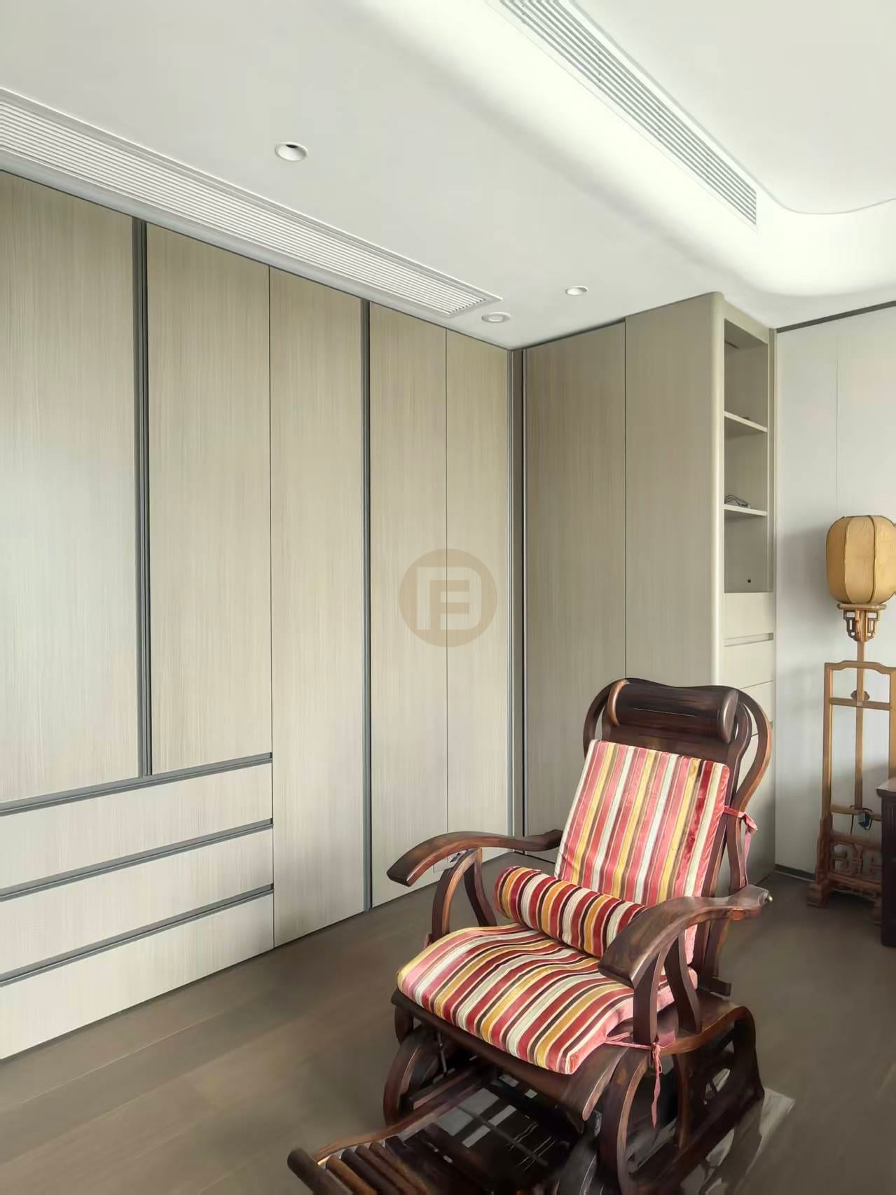 Floor-to-ceiling greige stainless steel wardrobe wall with recessed dark trims behind a rocking chair