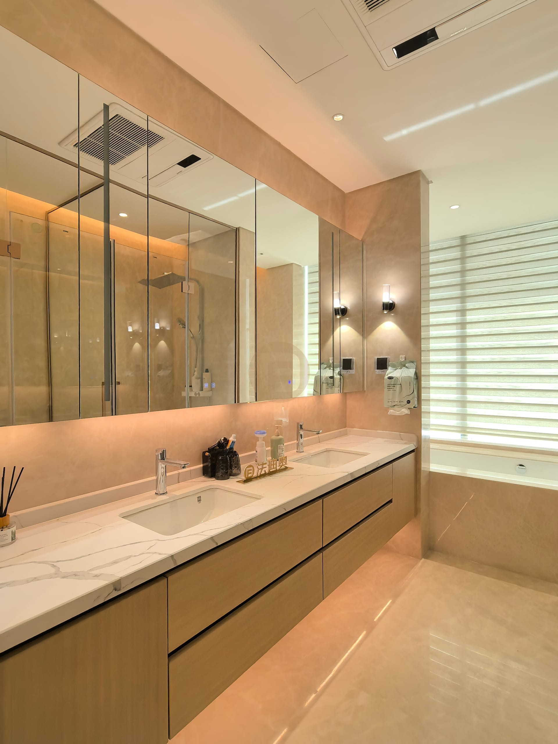 Twin-basin bathroom vanity in pale wood with a stone top beneath backlit mirror cabinets