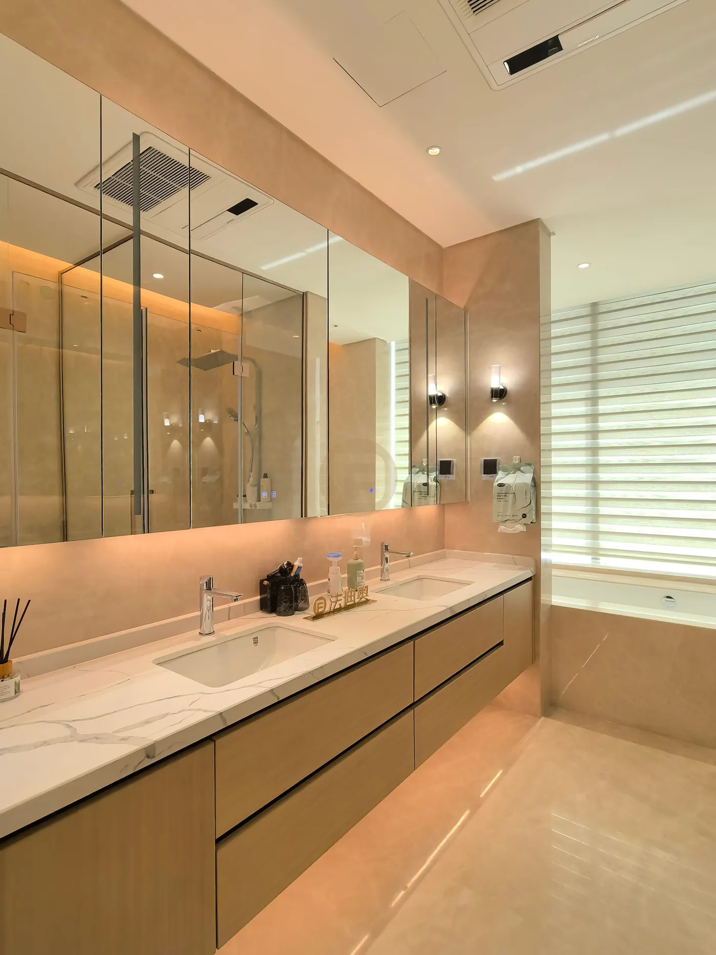 Twin-basin bathroom vanity in pale wood with a stone top beneath backlit mirror cabinets