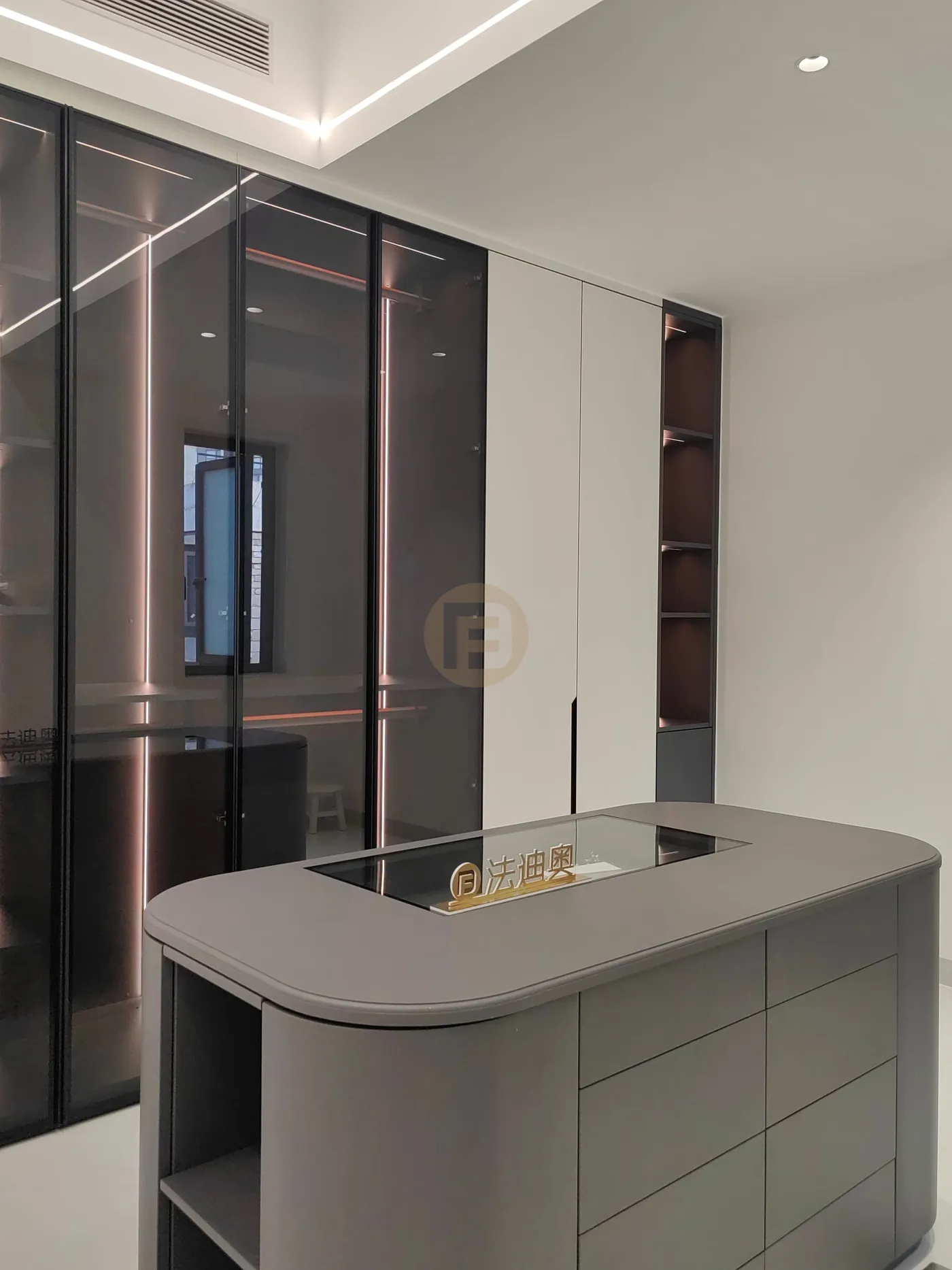 Walk-in closet with rounded grey island dresser and glass-front stainless steel wardrobes