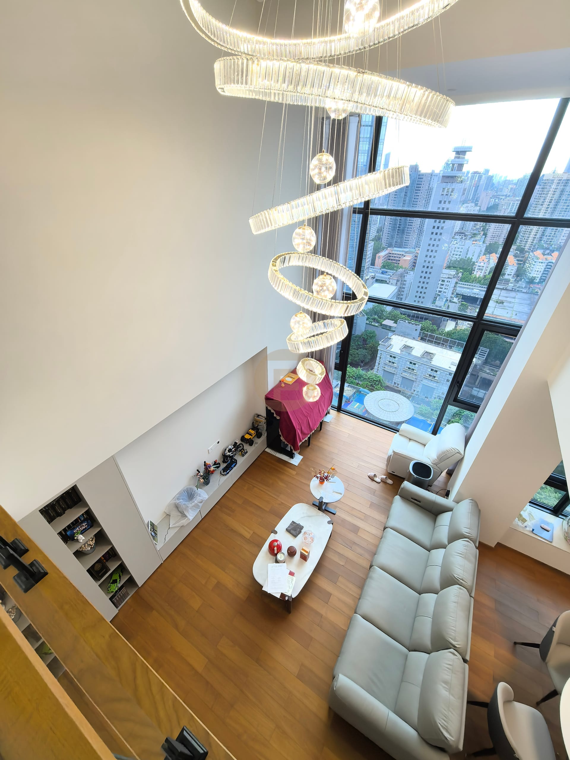 Double-height living room with tiered chandelier and floor-to-ceiling glazing over the city