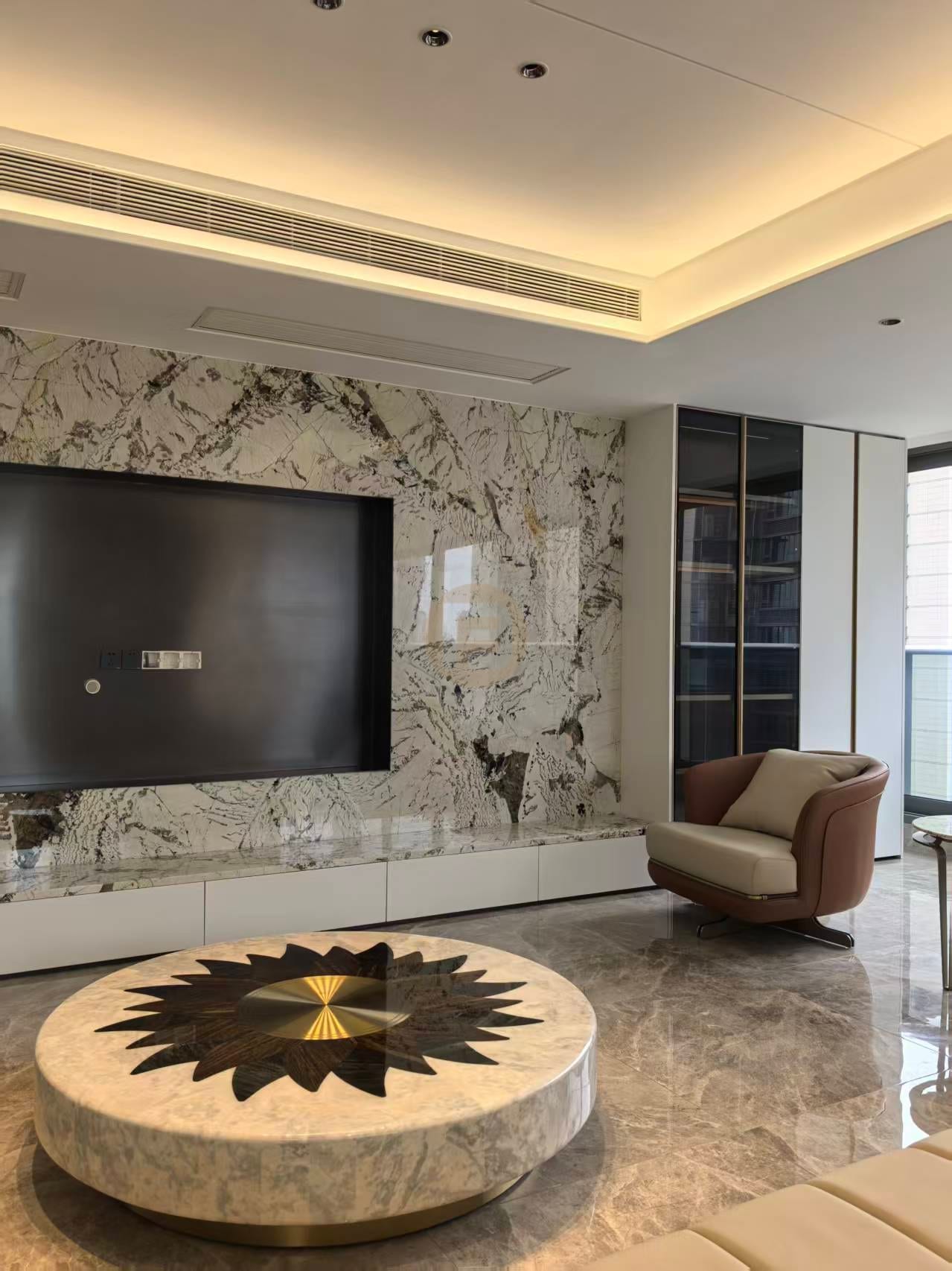 Marble media wall with white stainless steel base cabinets, sunburst stone coffee table and leather armchair