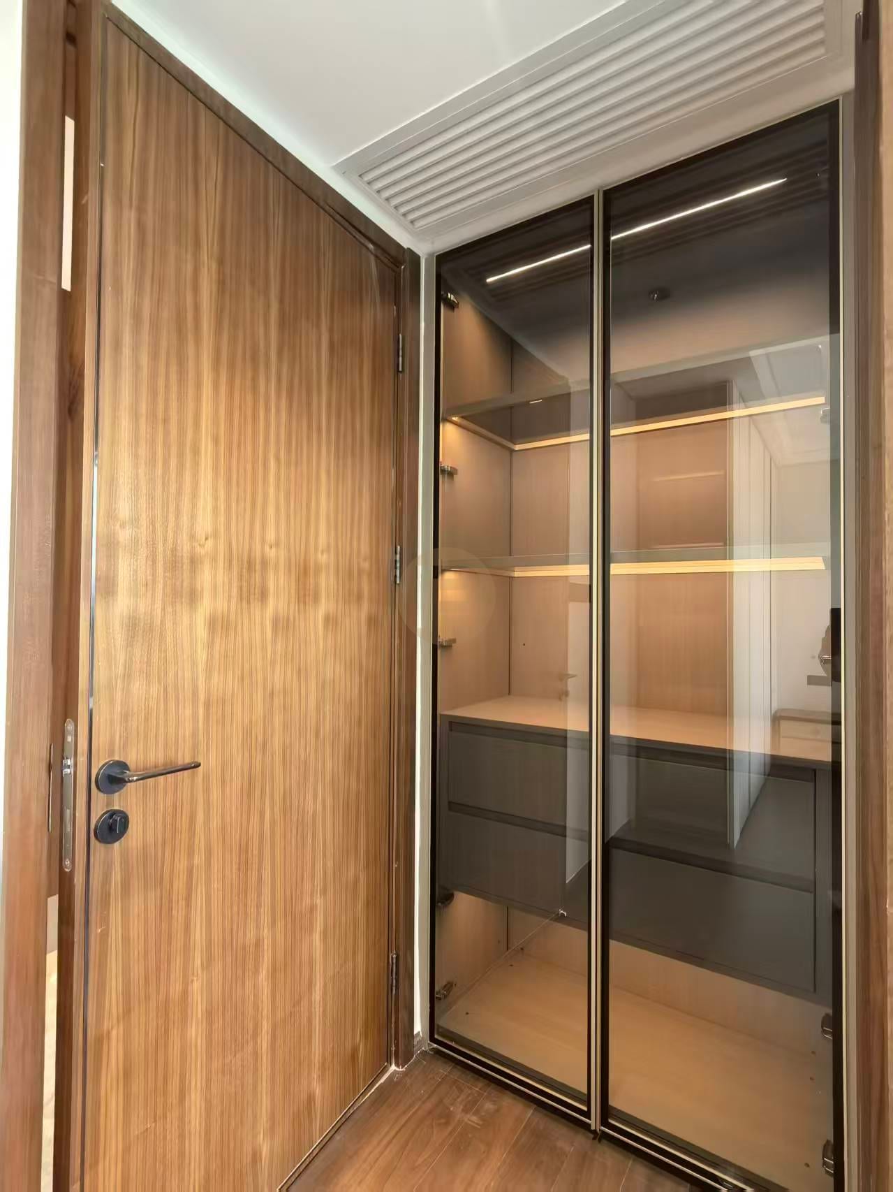 Entryway with walnut door beside a bronze-glass pantry cabinet with lit interior shelving