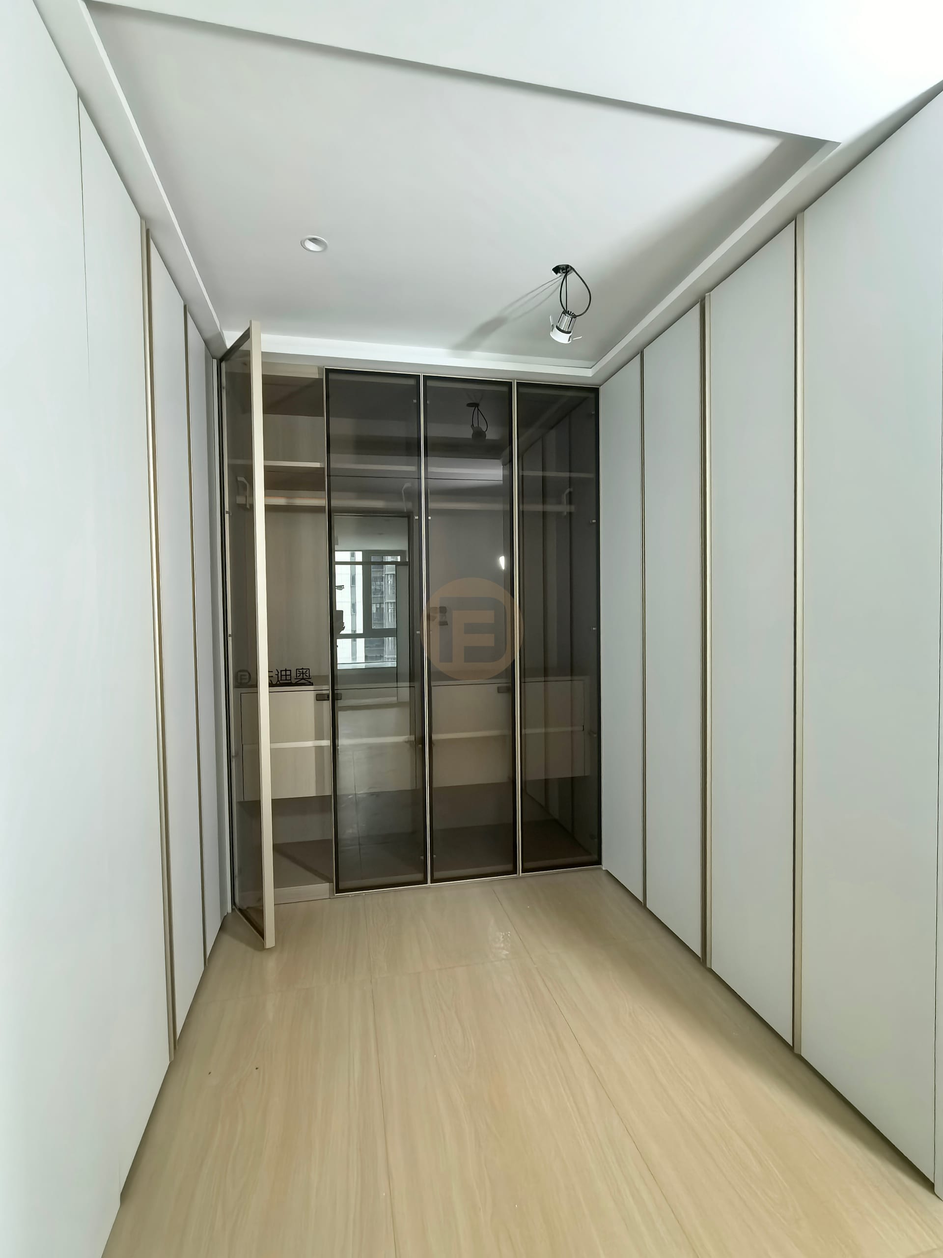 Dressing corridor lined with champagne-trimmed white wardrobes ending in a smoked-glass display cabinet