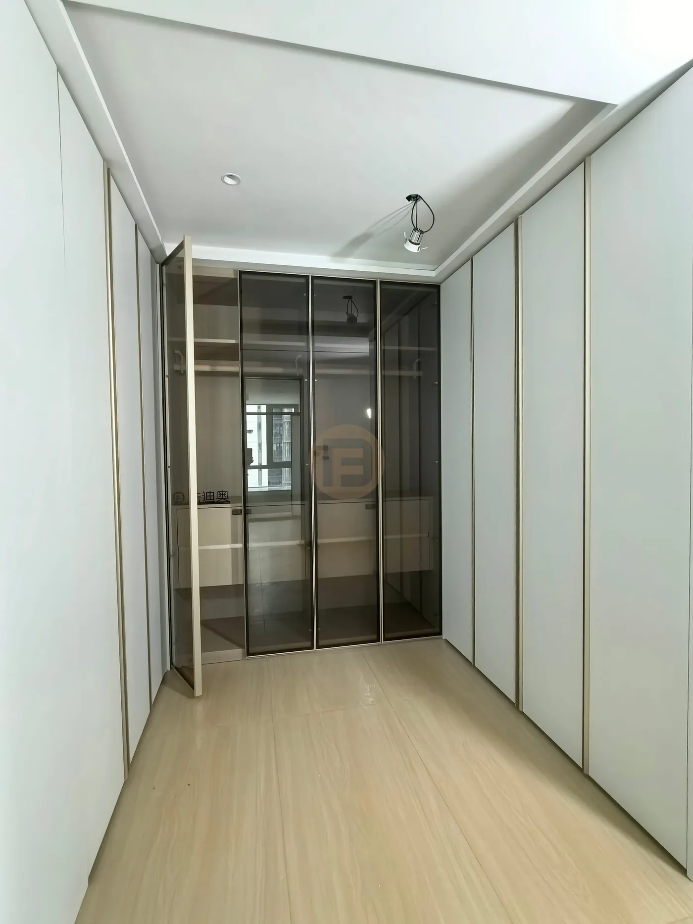Dressing corridor lined with champagne-trimmed white wardrobes ending in a smoked-glass display cabinet