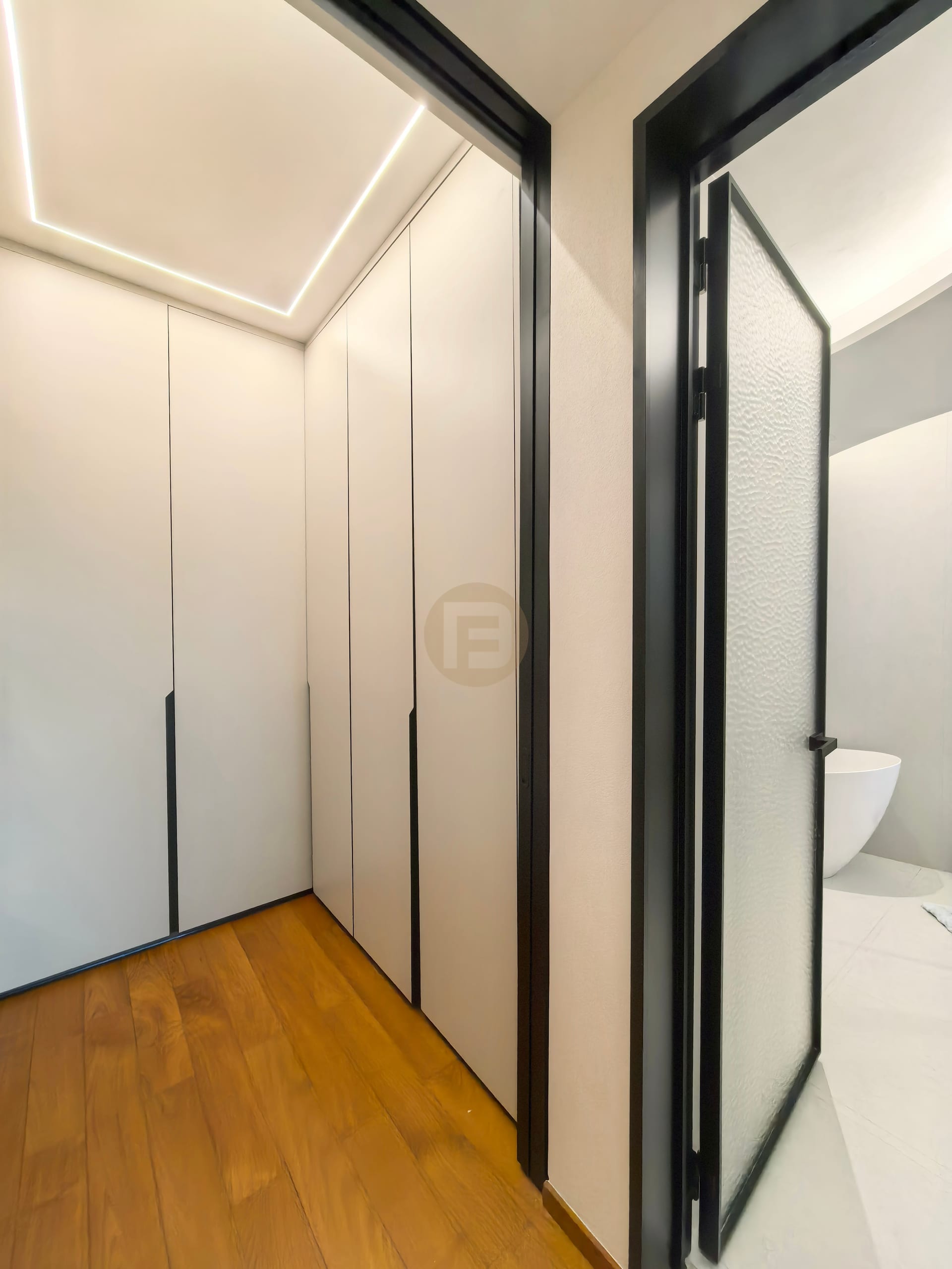 Corridor wardrobes with recessed black handles beside a black-framed glass bathroom door