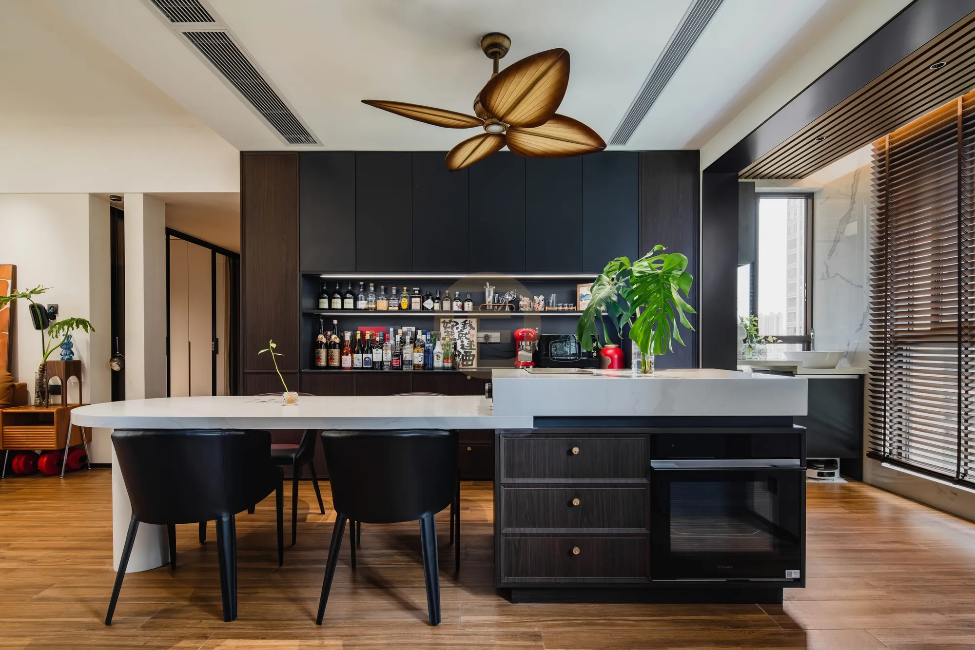 Black stainless steel kitchen island and full-height bar cabinetry with backlit shelving under a rattan ceiling fan