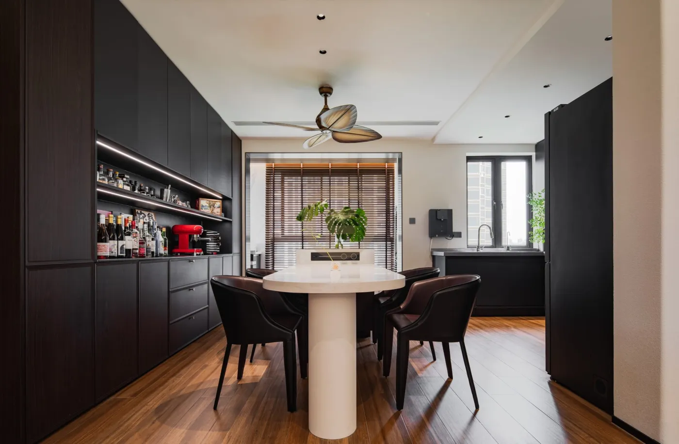 Oval dining table before a matte black stainless steel bar wall with backlit shelving and integrated drawers