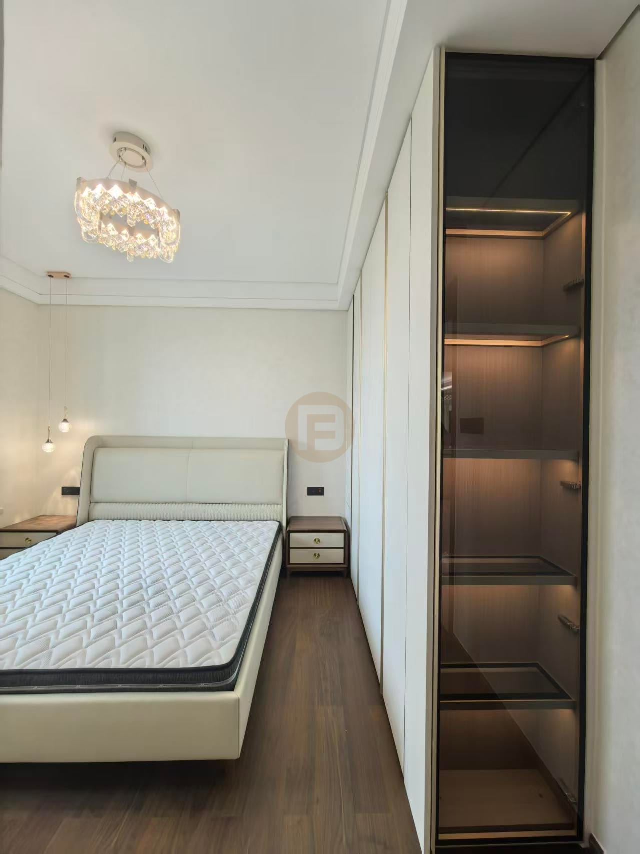 Primary bedroom with cream stainless steel wardrobe wall, smoked-glass display column and crystal chandelier