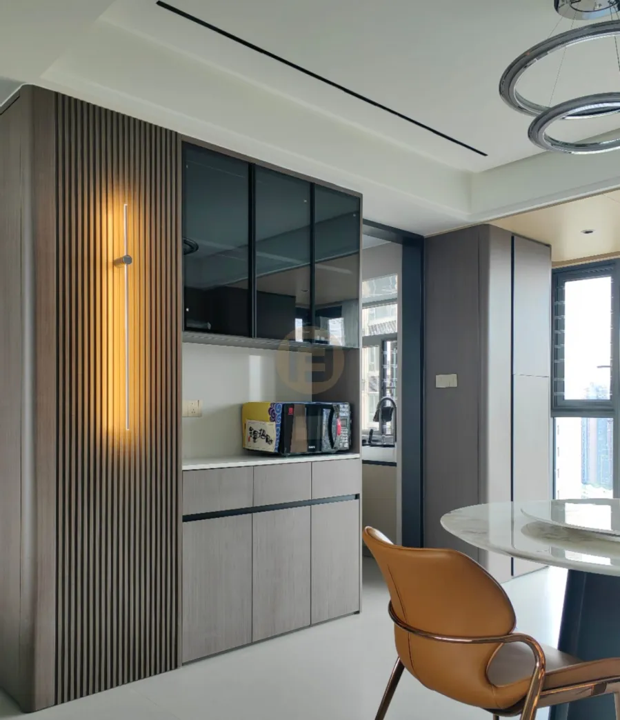 Dark wood-grain stainless steel sideboard with lit fluted panel and smoked-glass cabinets beside a round marble dining table