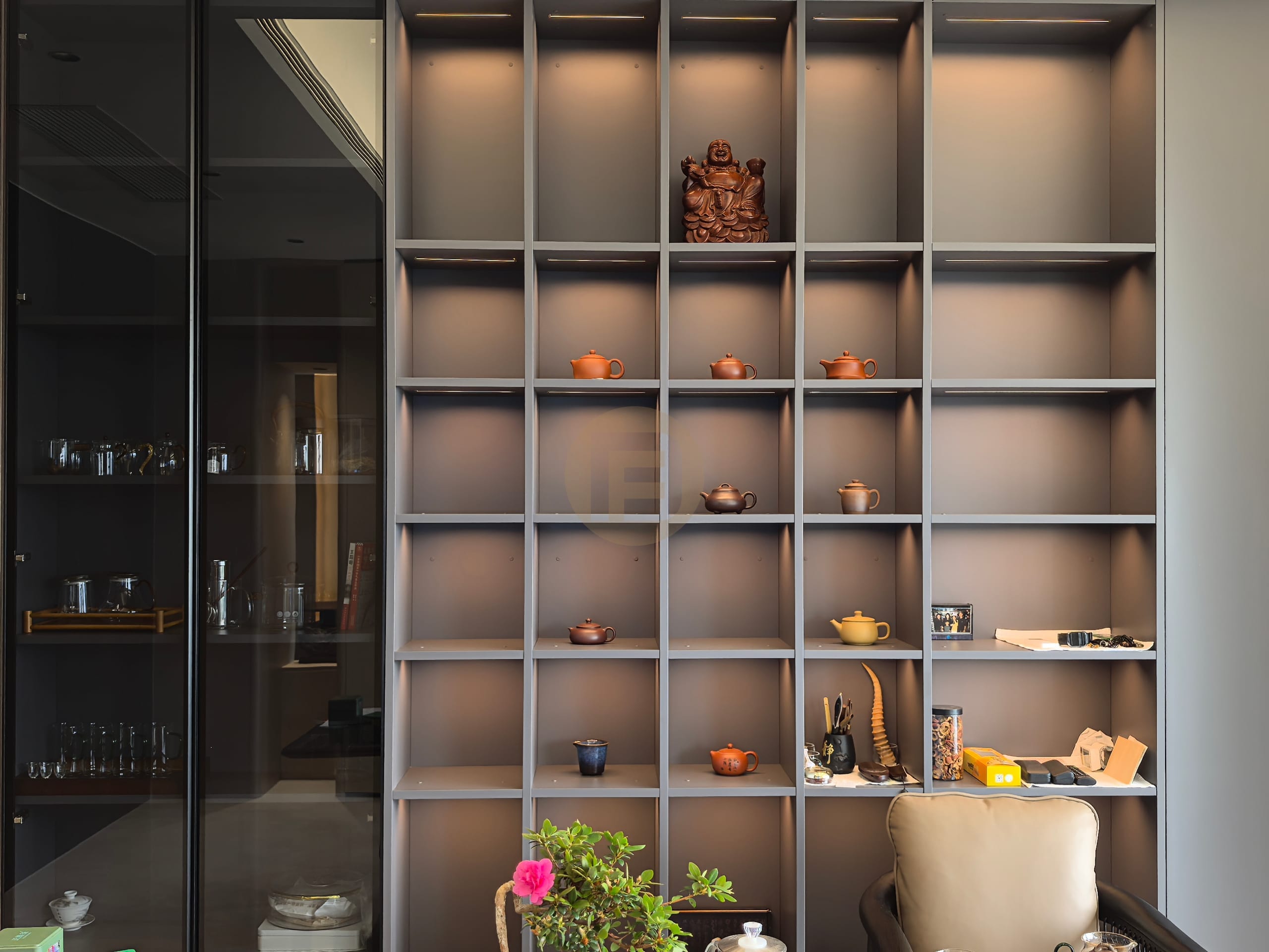 Backlit tea room shelving styled with clay teapots beside a smoked-glass storage cabinet