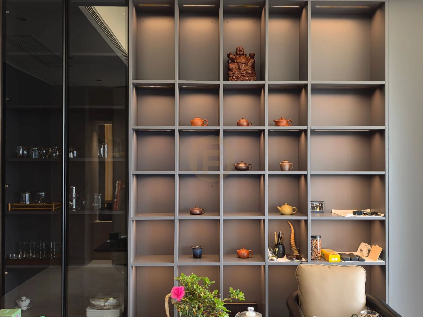 Backlit tea room shelving styled with clay teapots beside a smoked-glass storage cabinet