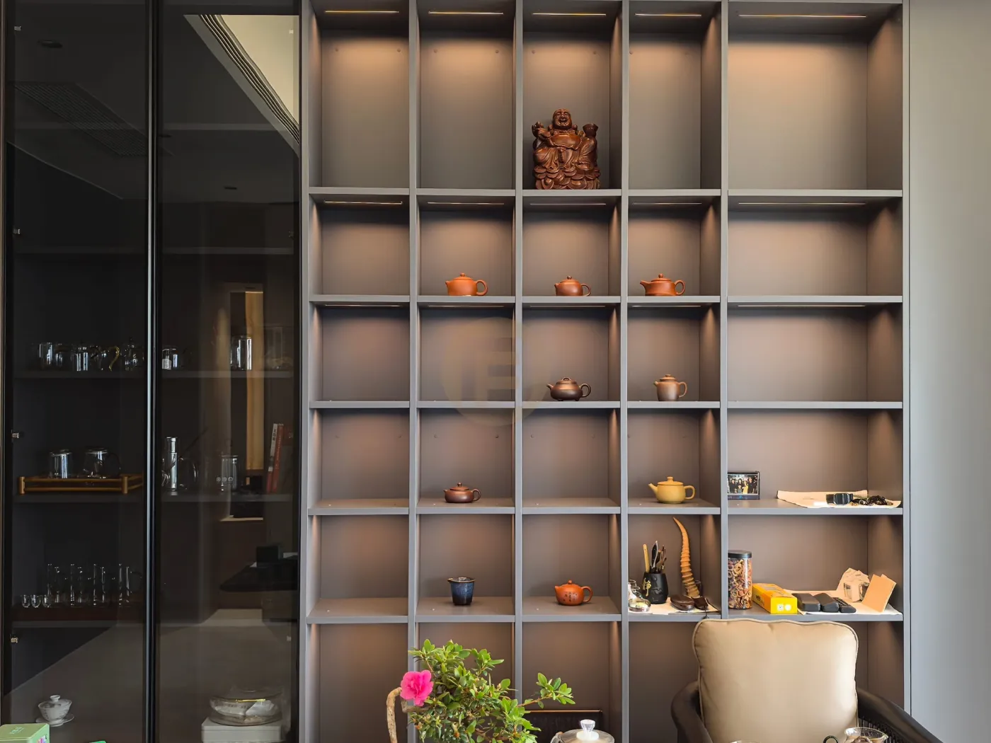 Backlit tea room shelving styled with clay teapots beside a smoked-glass storage cabinet
