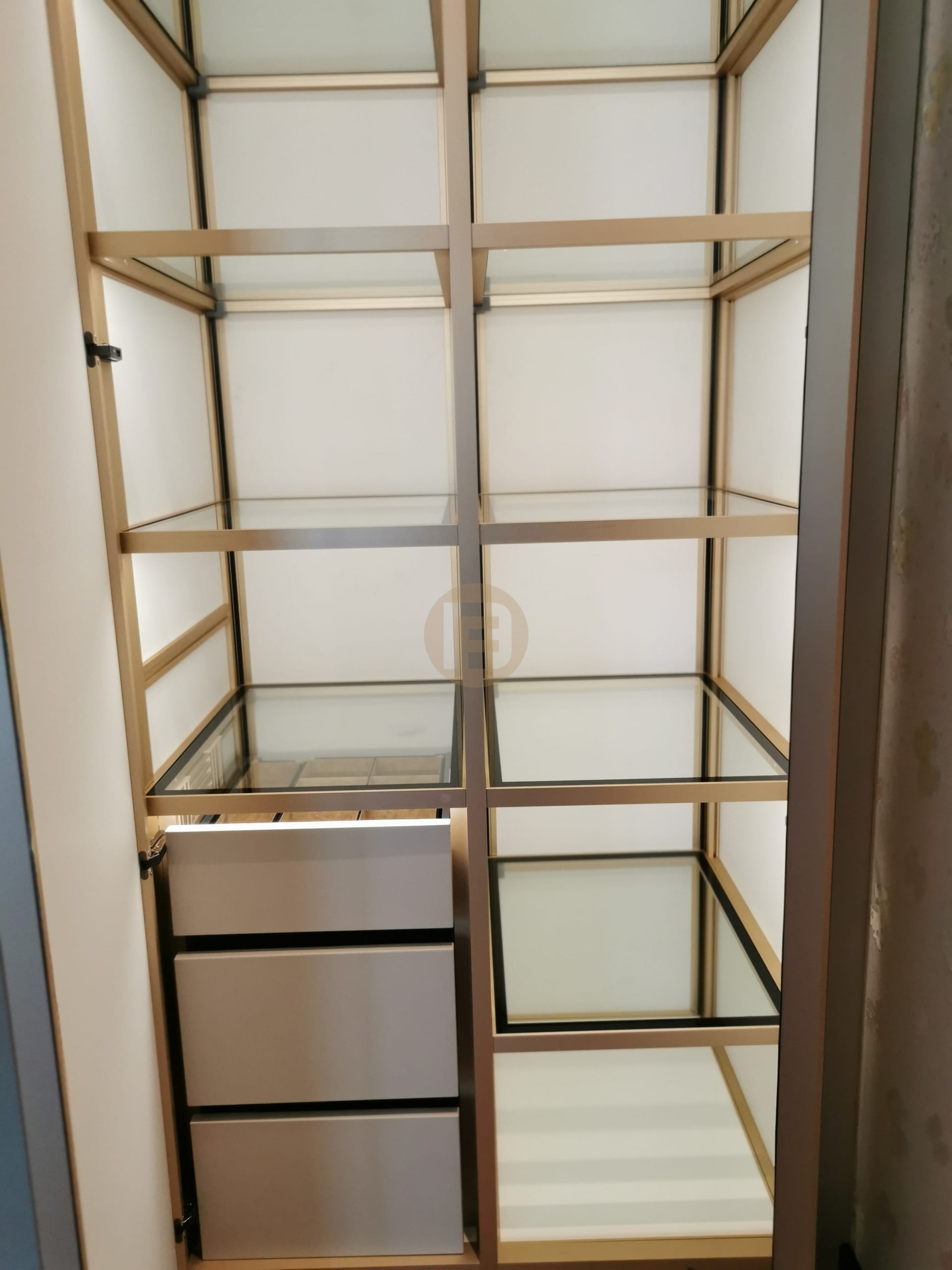 Wardrobe interior with gold-framed glass shelf levels and a stack of silver-faced stainless steel drawers