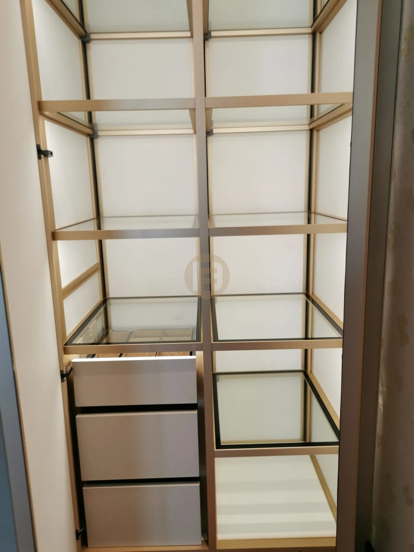 Wardrobe interior with gold-framed glass shelf levels and a stack of silver-faced stainless steel drawers