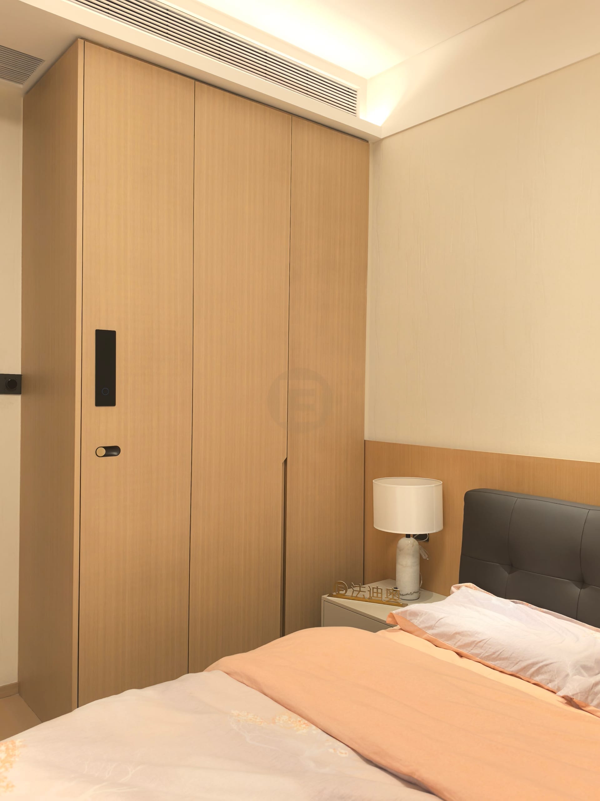 Light woodgrain stainless steel wardrobe with recessed black handles in a guest bedroom