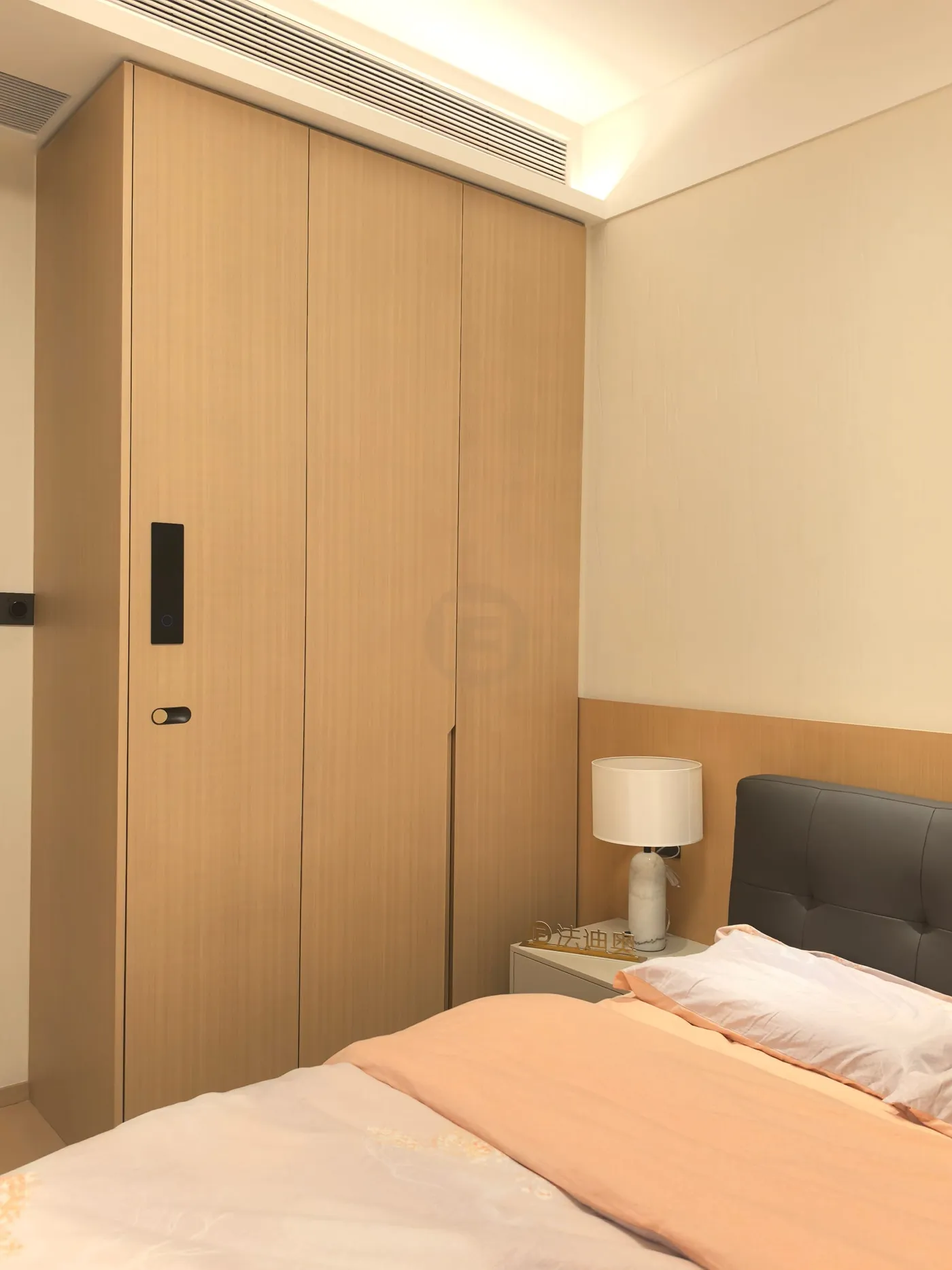 Light woodgrain stainless steel wardrobe with recessed black handles in a guest bedroom