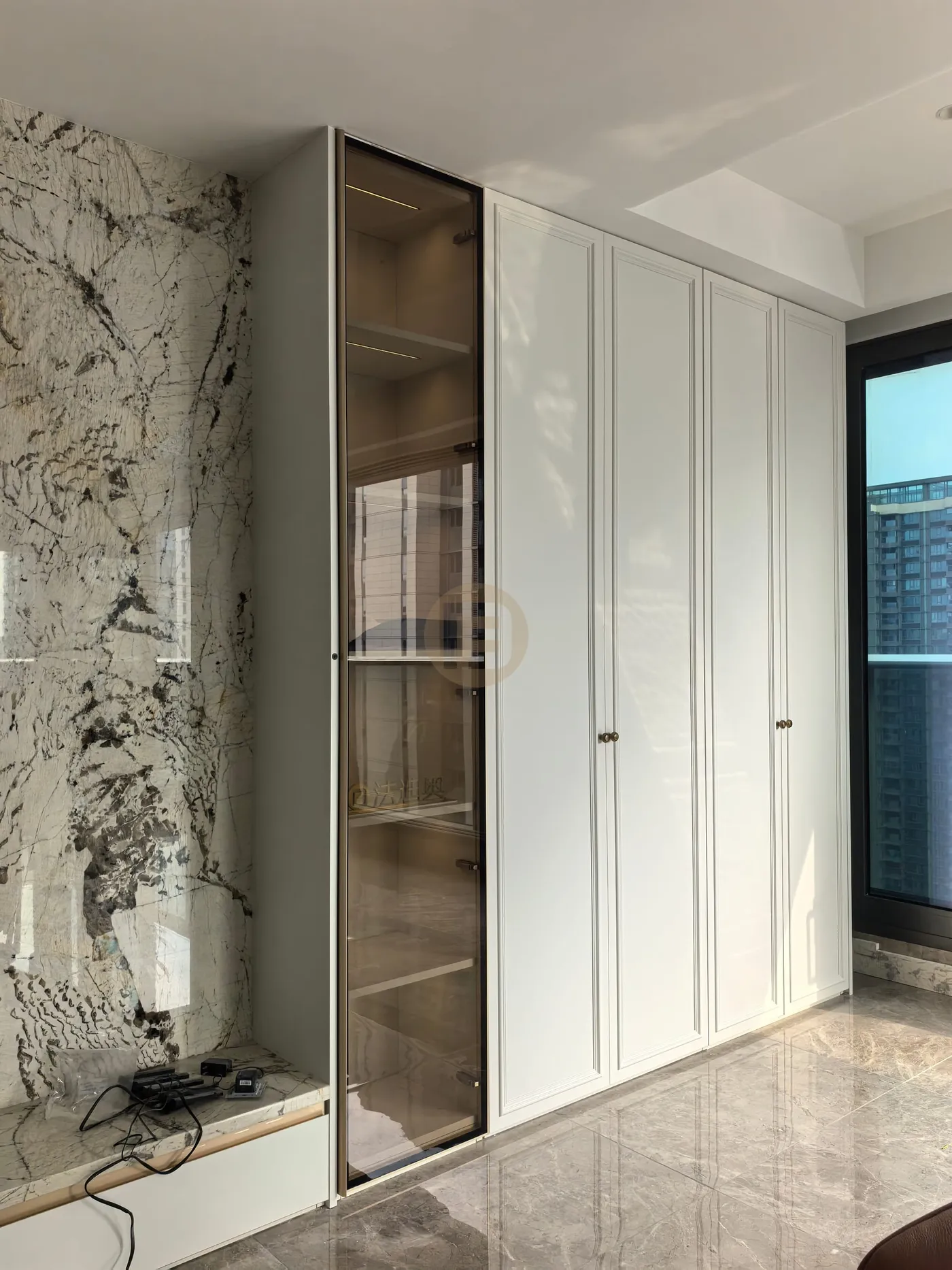 White paneled stainless steel cabinetry with a bronze glass display column beside a veined marble feature wall
