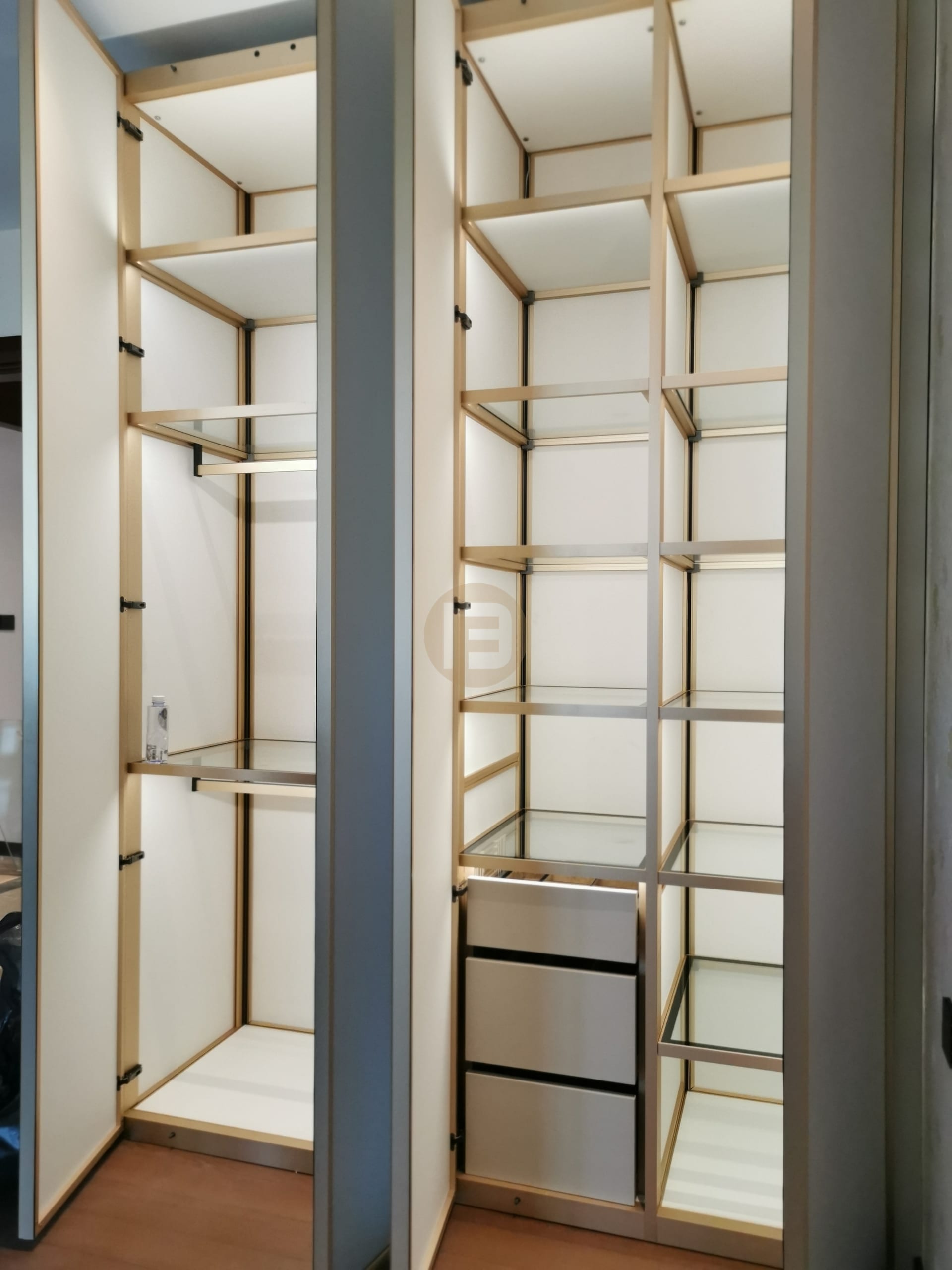 Open stainless steel wardrobe columns with champagne-gold framing, glass shelves and hanging rails