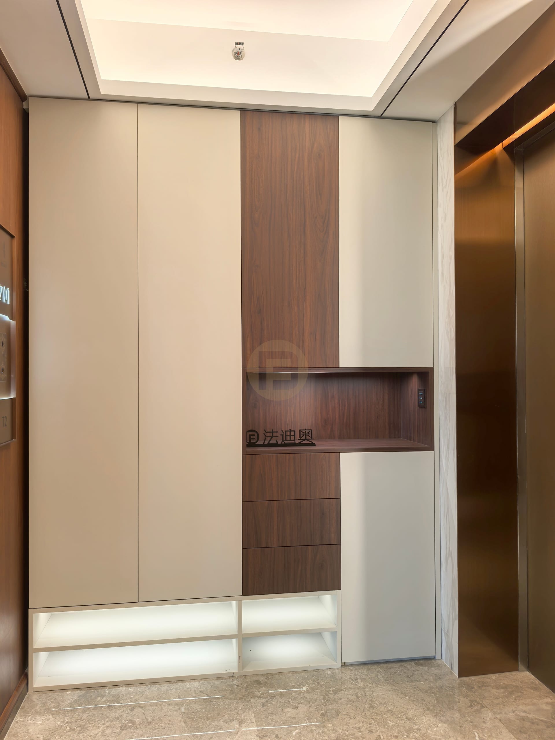 Entry storage in cream stainless steel cabinetry with a lit walnut display niche